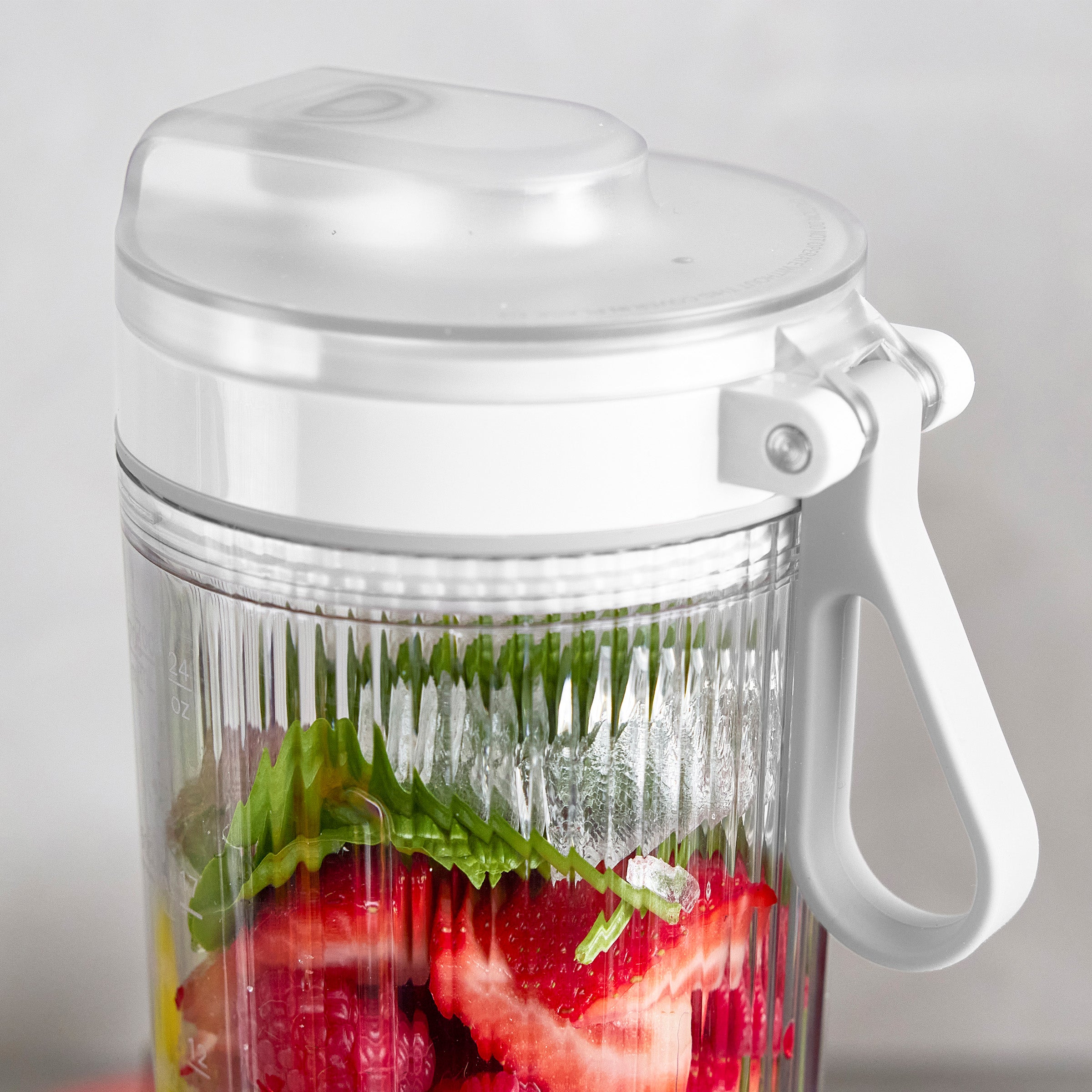 Blender jar with strawberries and greens on a light gray background