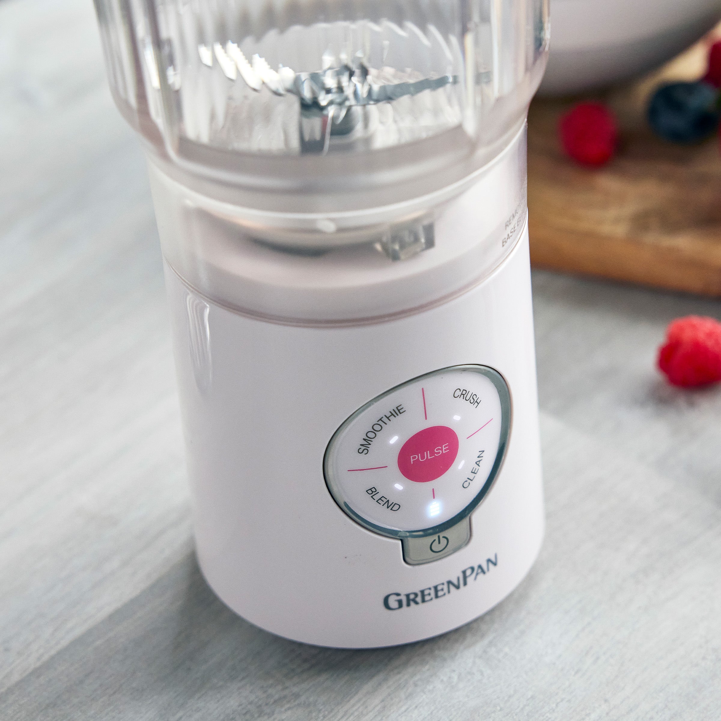 Pink blender with control panel on a light gray surface, surrounded by berries.