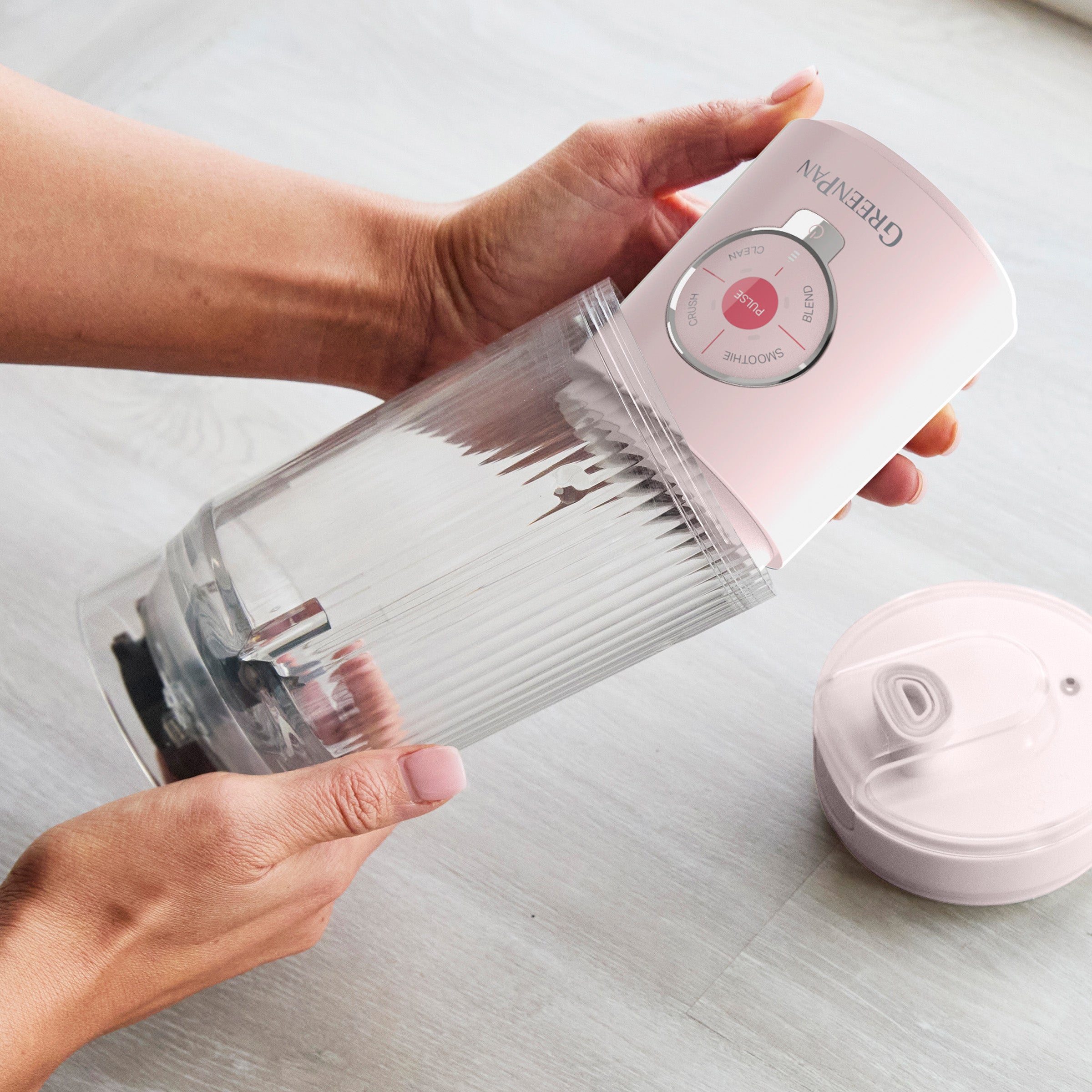Person holding a pink and clear portable blender on a light surface