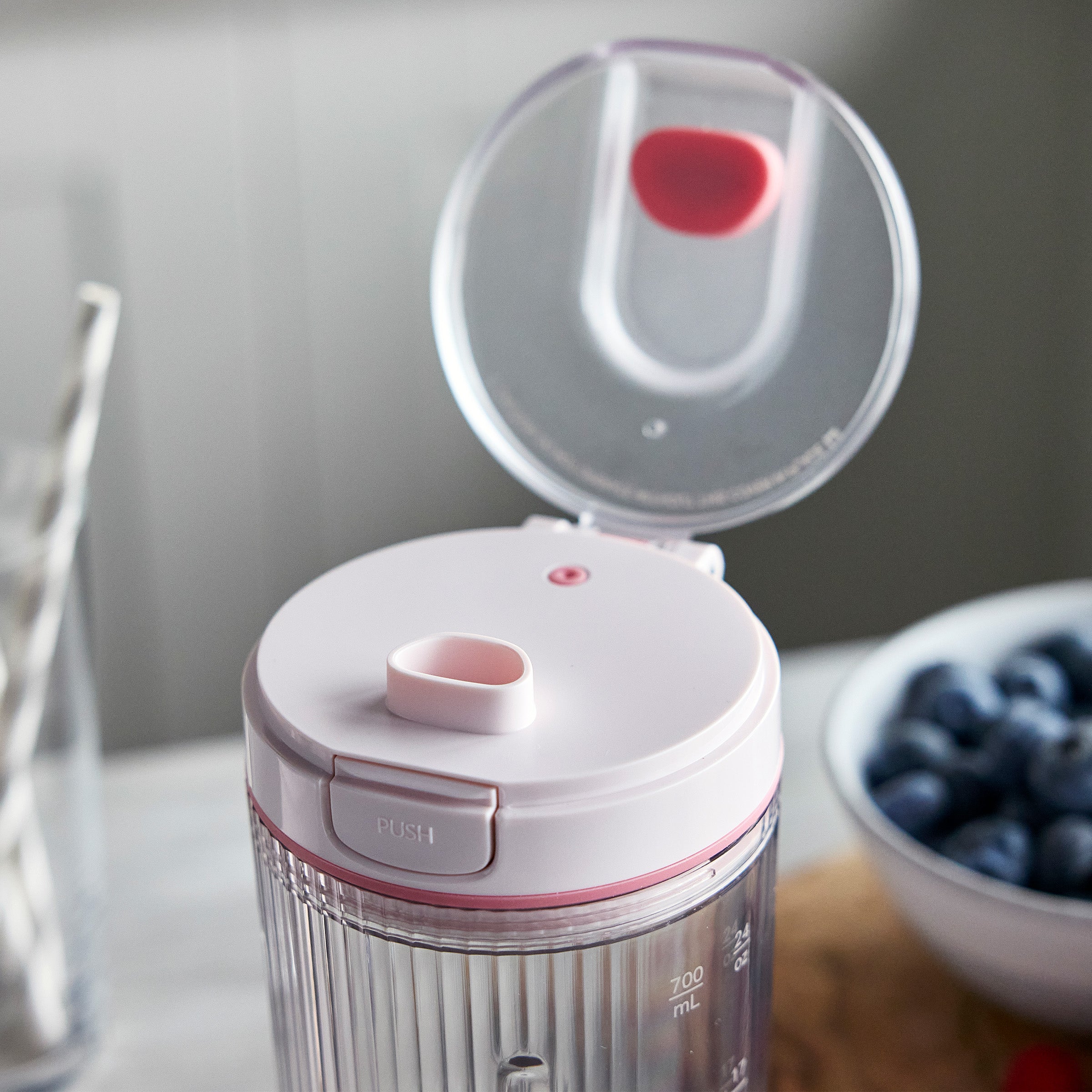 White and pink portable blender with a bowl of blueberries in the background