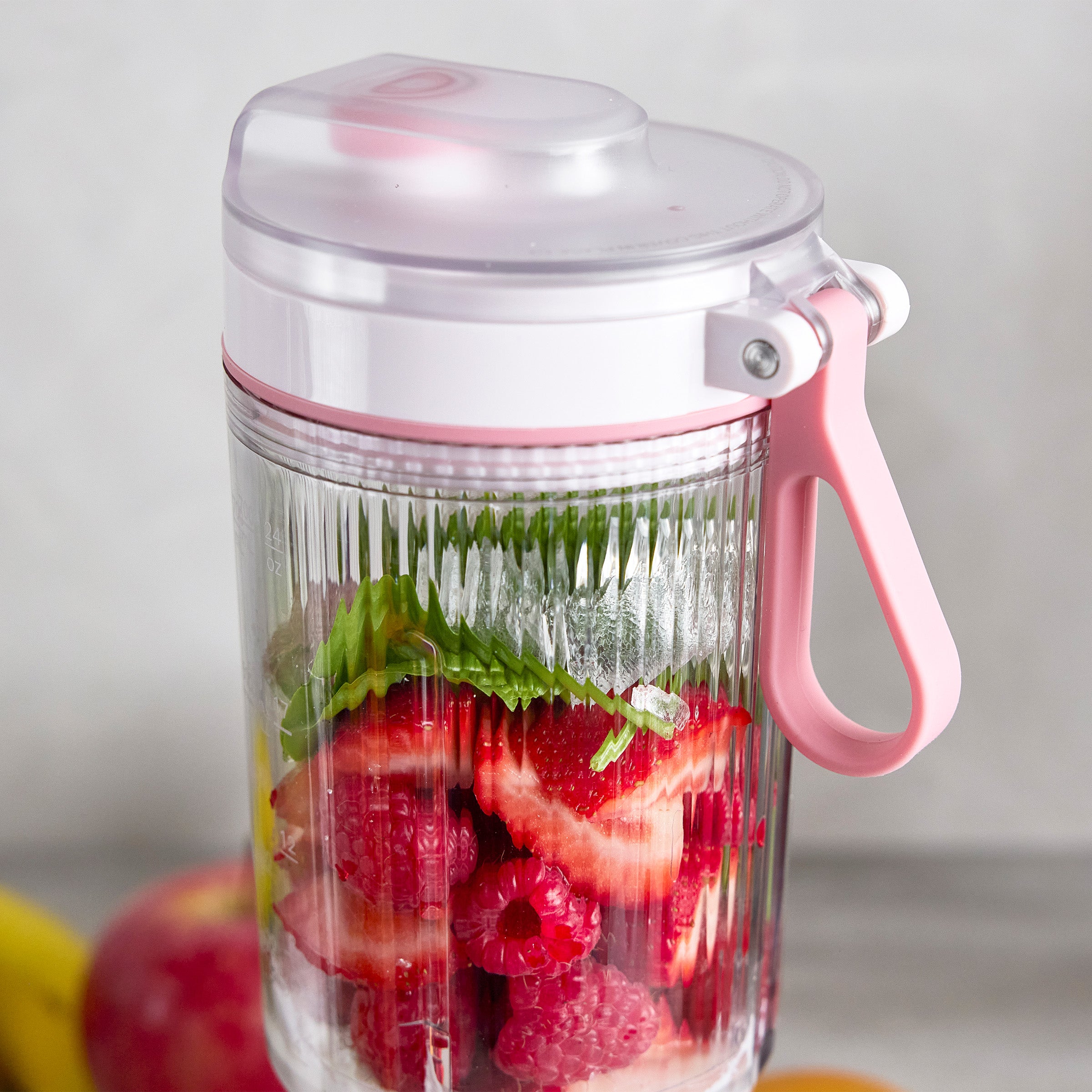 Pink portable blender filled with strawberries and raspberries on a light background