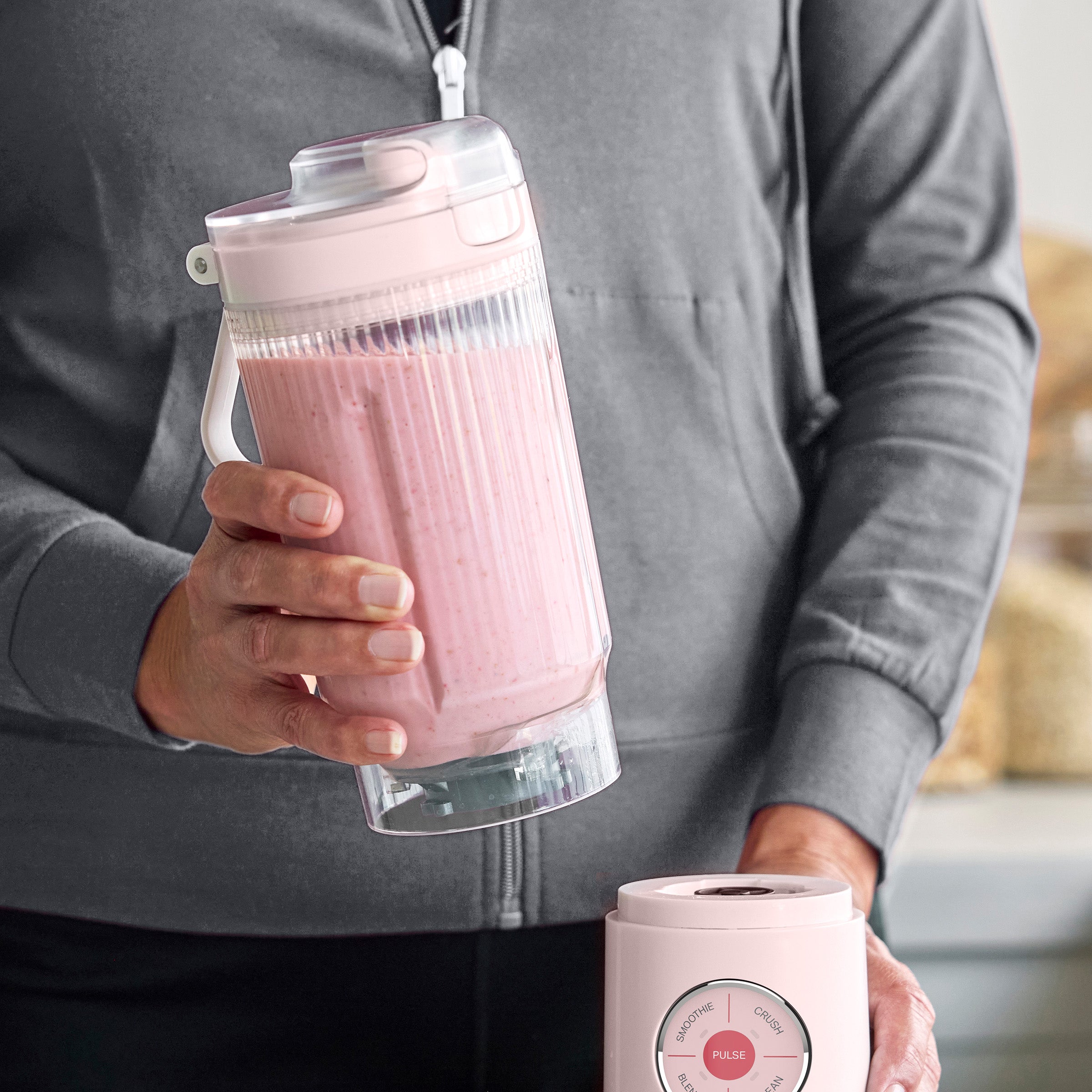 Person holding a pink portable blender with a pink smoothie inside, blurred background