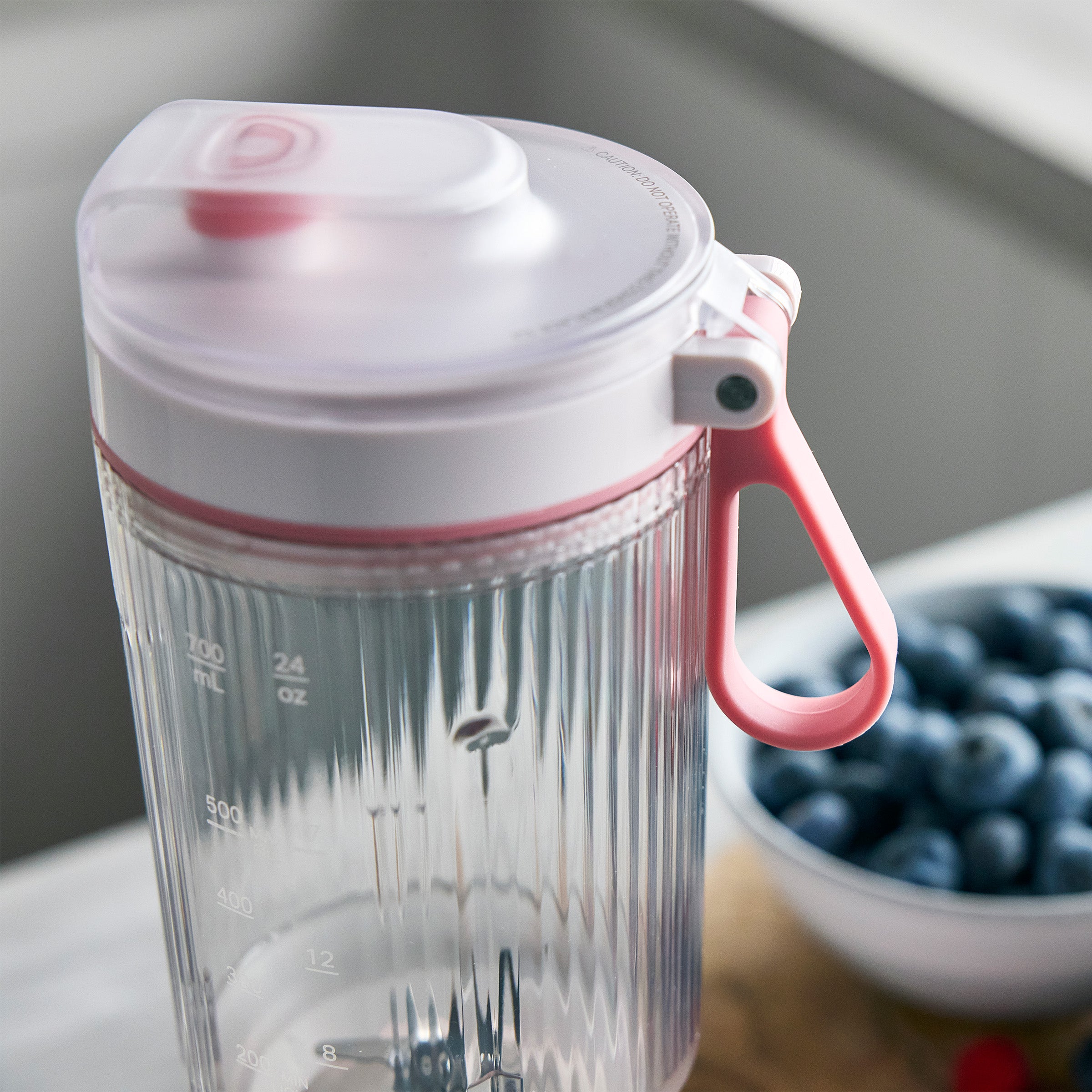 Clear blender container with pink handle and lid on a blurred background