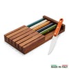 Six steak knives with multicolor handles arranged in a wooden tray.