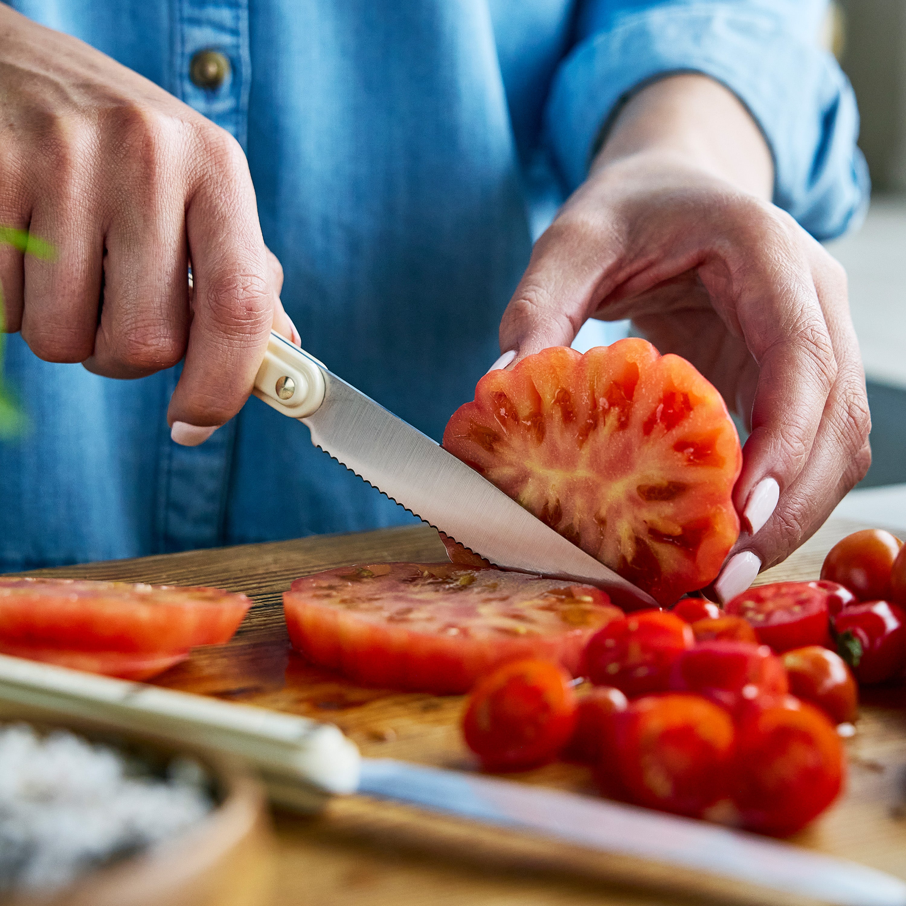 Person cutting tomatoes on a wooden board with a knife