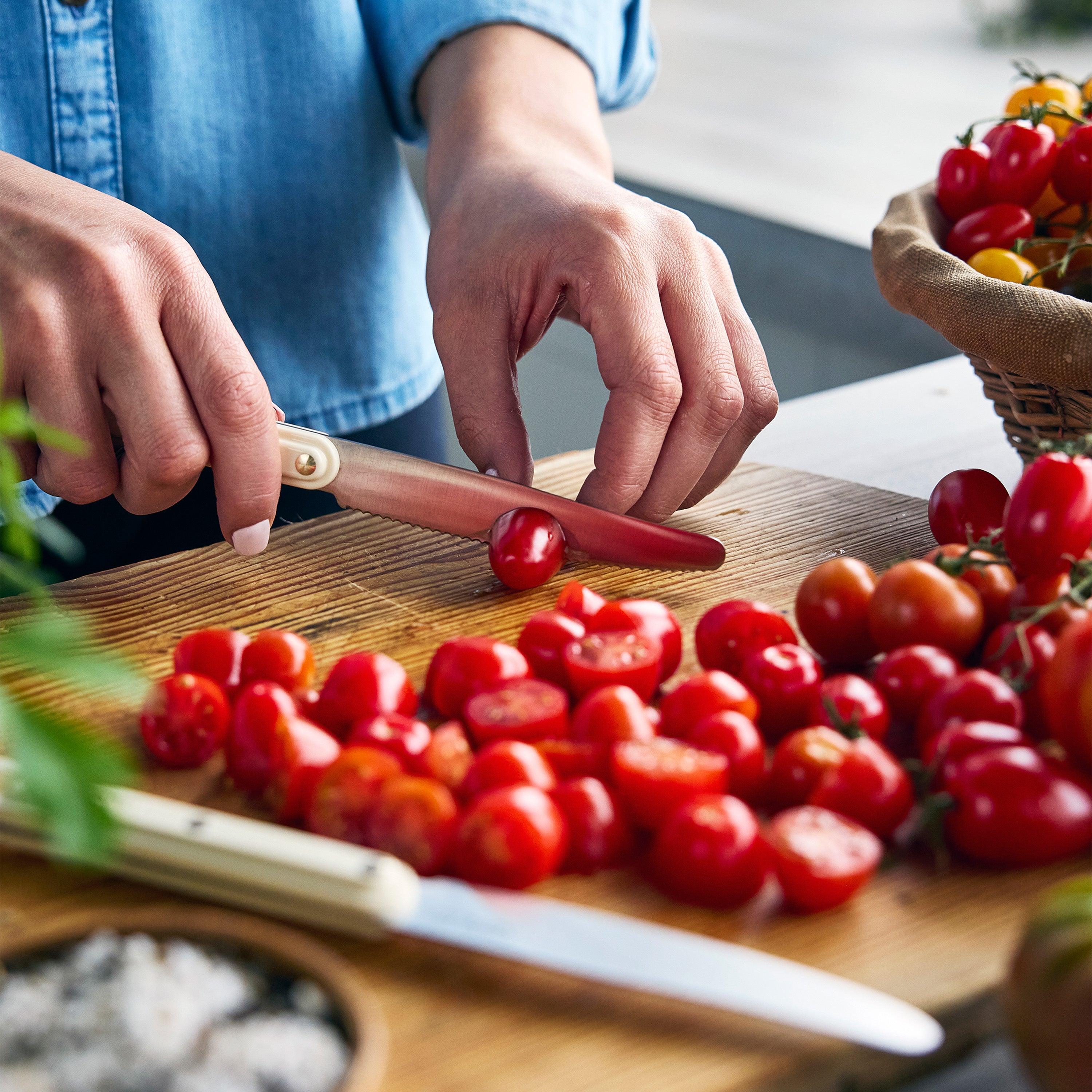 Person cutting cherry tomatoes on a wooden board with a knife.