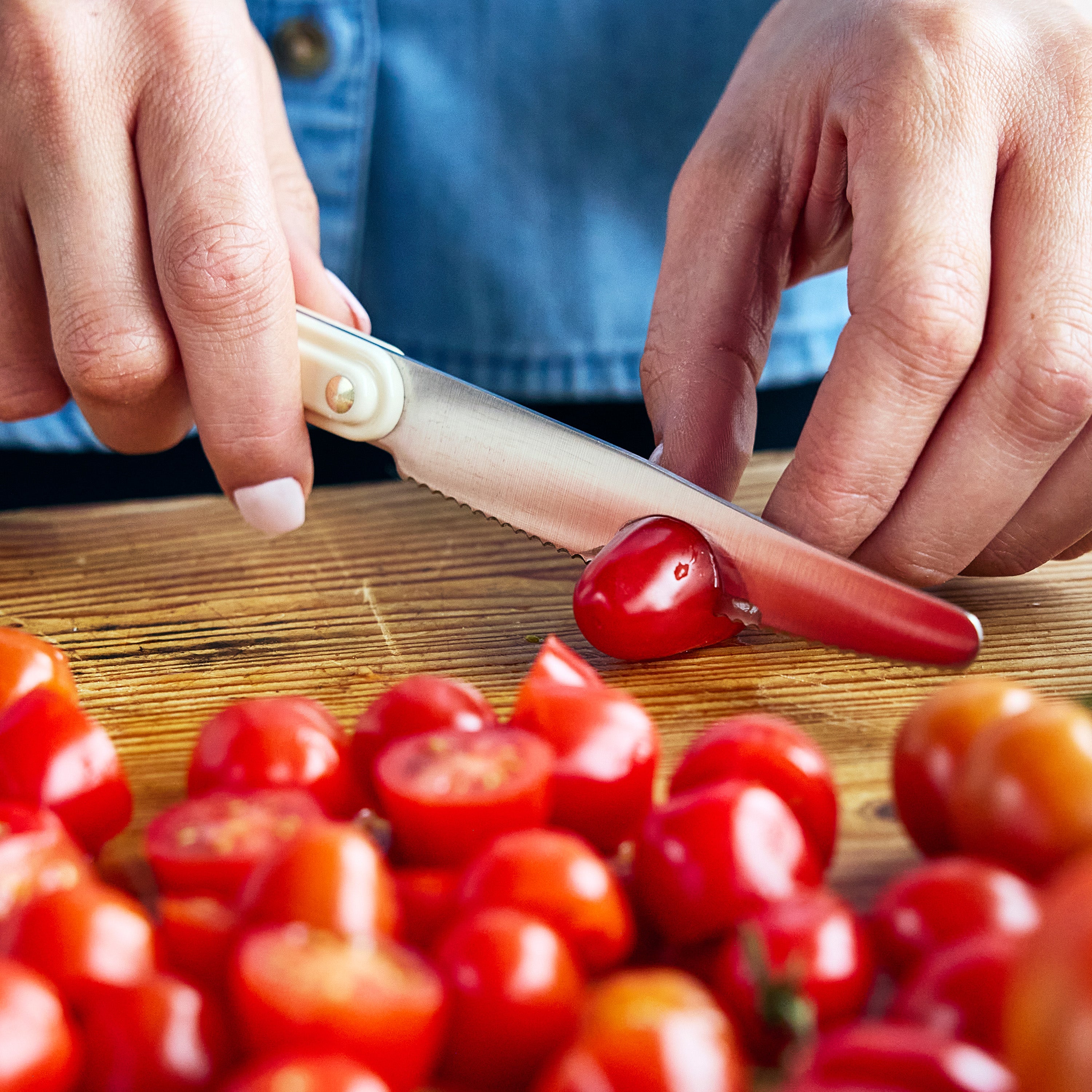 Person cutting cherry tomatoes on a wooden board with a knife.