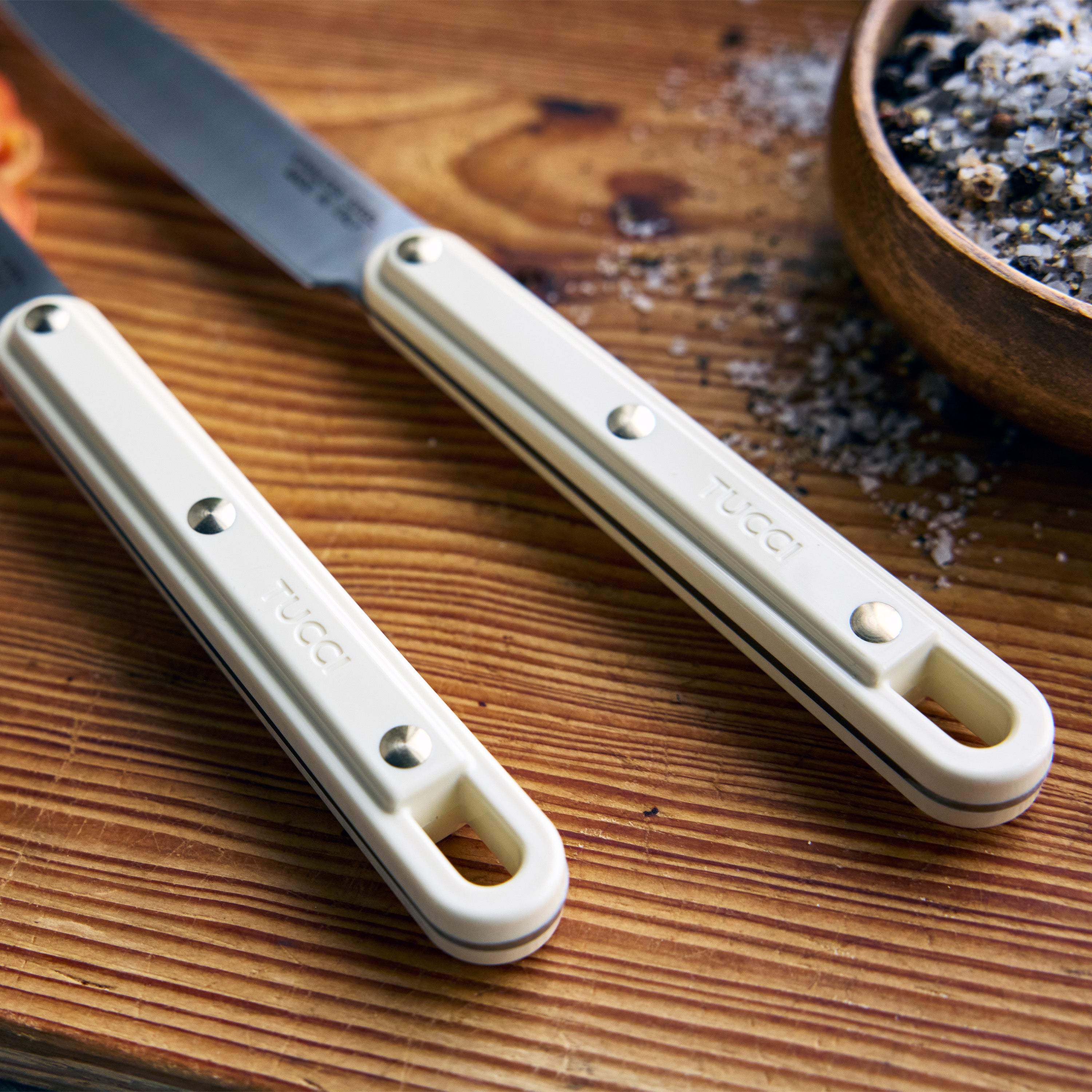 Knife with a white handle on a wooden surface next to a wooden bowl.