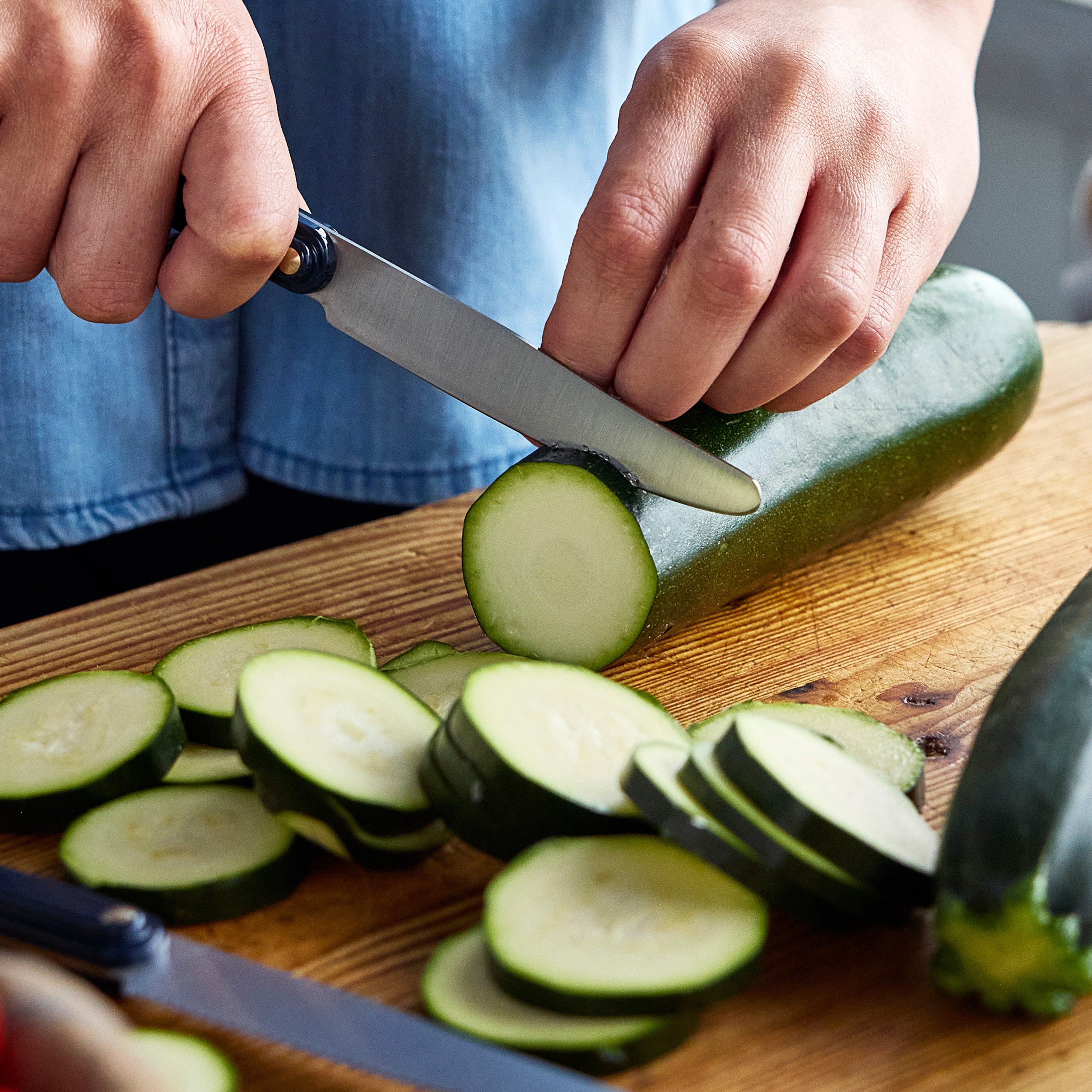 Person slicing zucchini on a wooden cutting board with a knife.