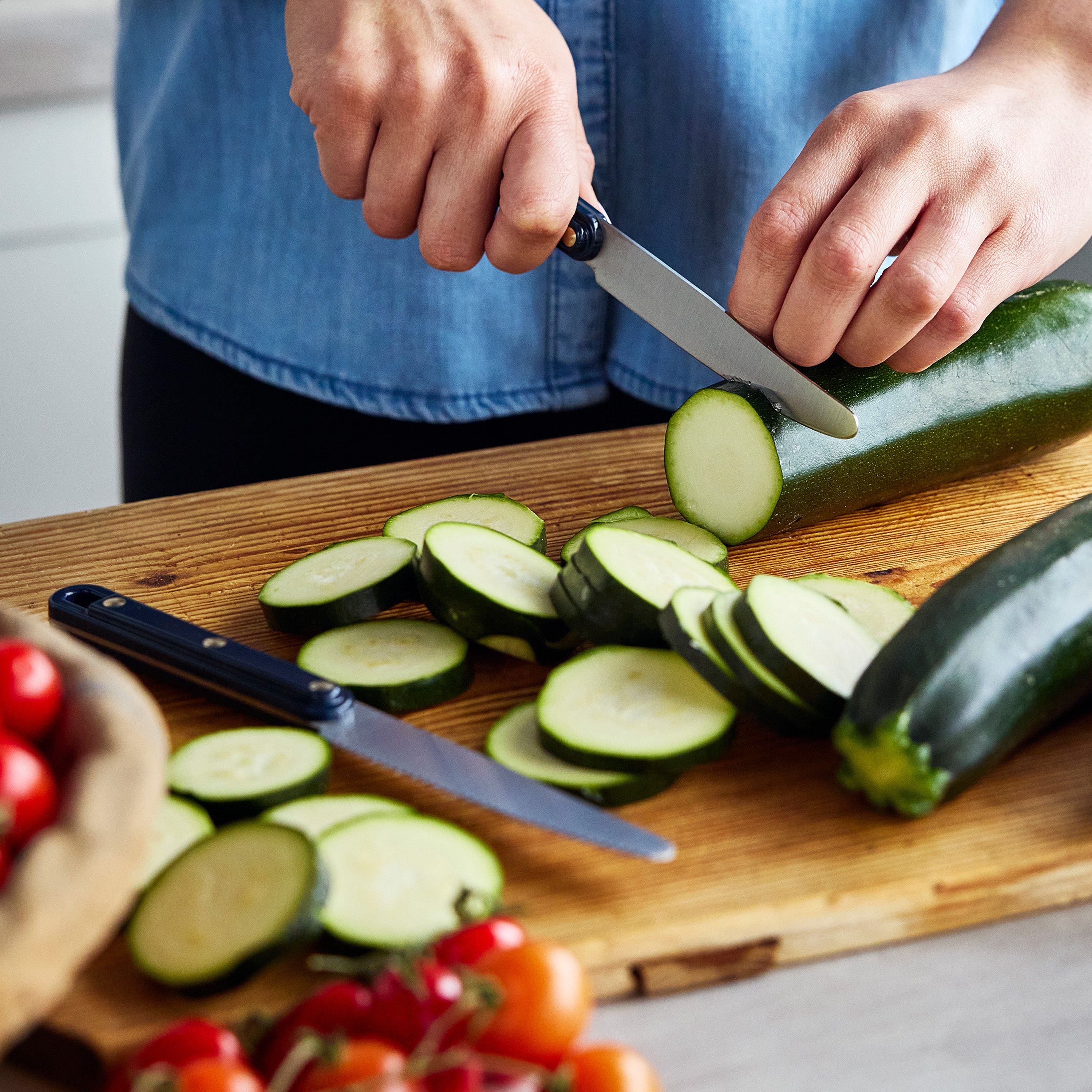 Person slicing zucchini on a wooden cutting board with a knife.
