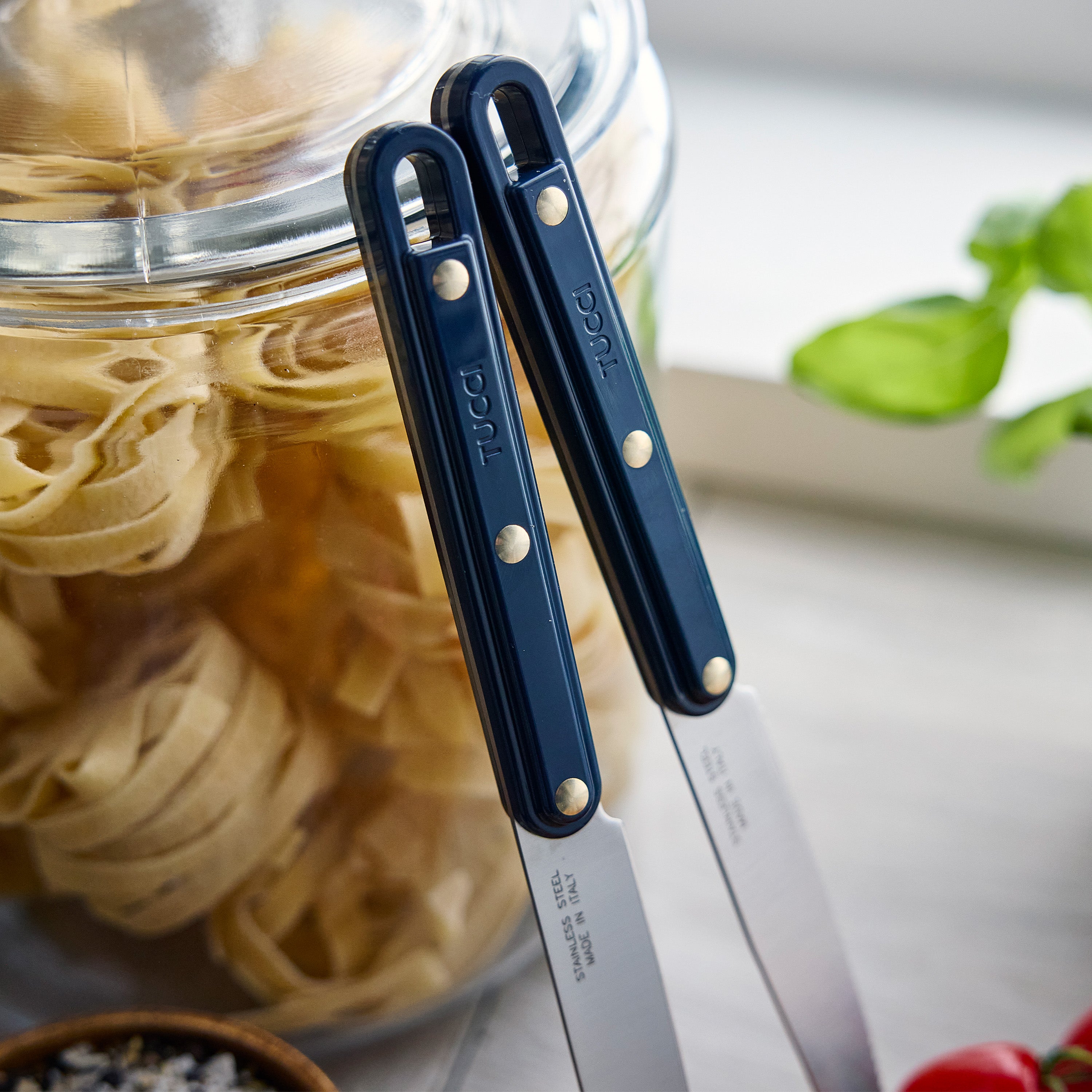 Two knives with blue handles next to a jar of pasta.