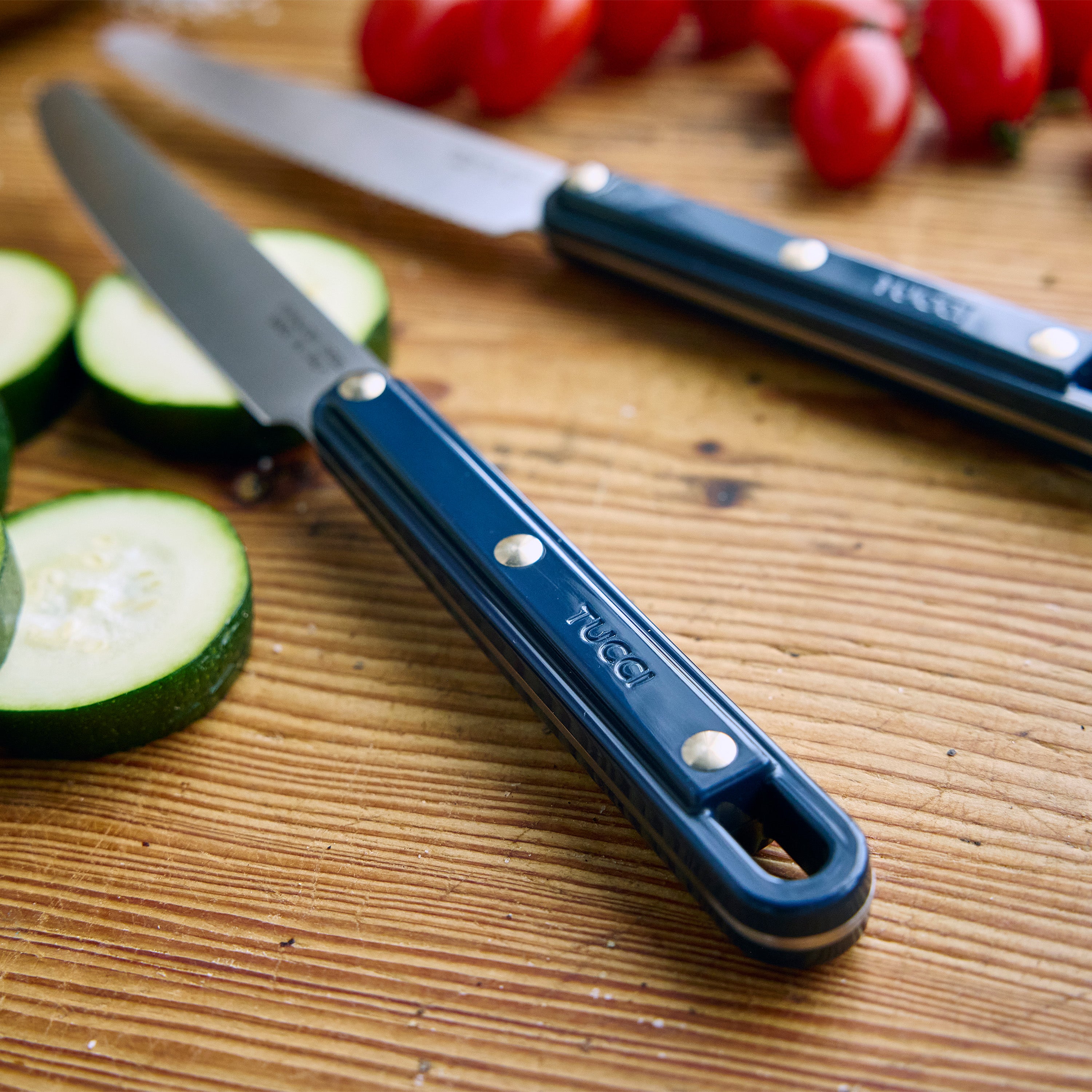 Blue kitchen knives on a wooden surface with vegetables
