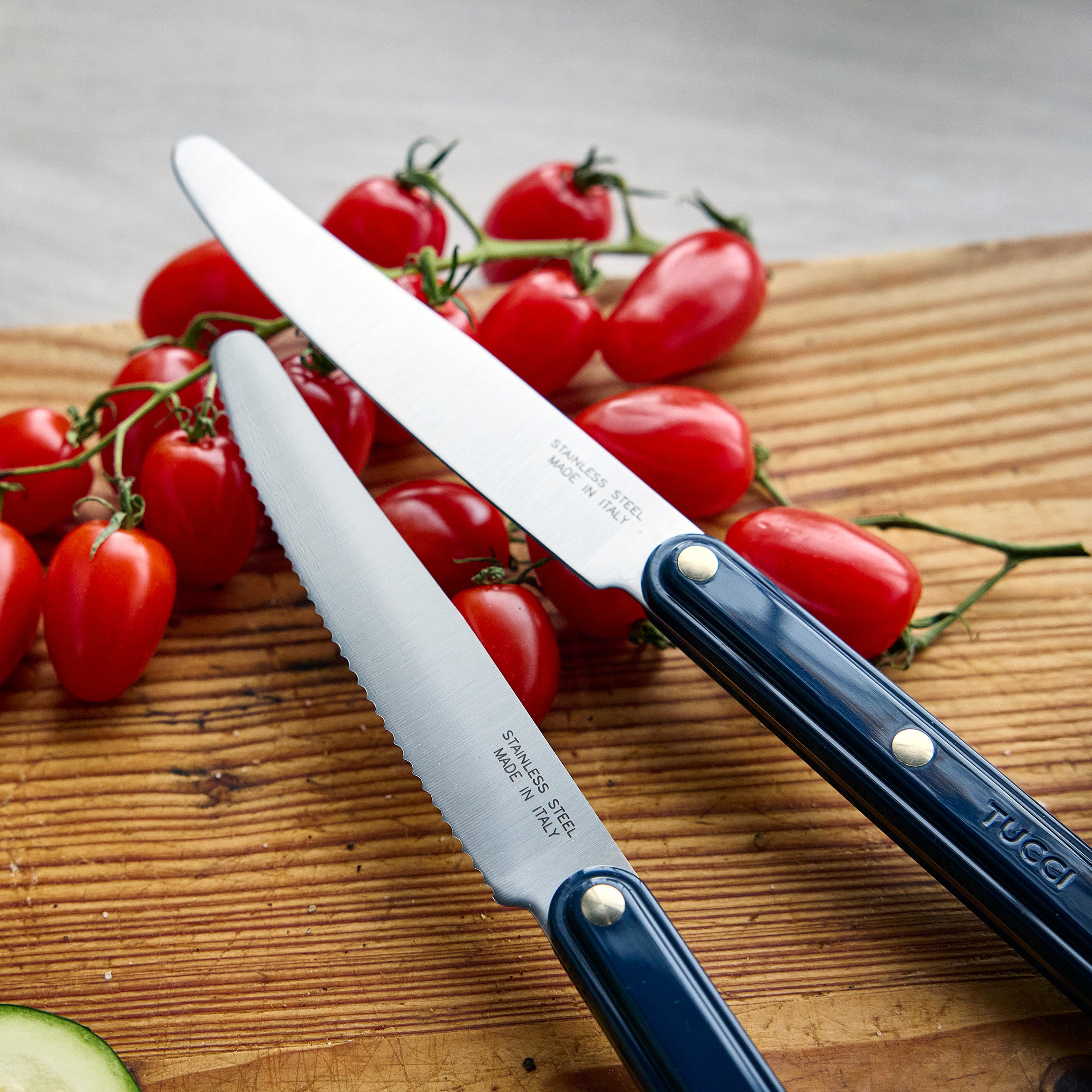 Two knives with blue handles on a wooden cutting board with tomatoes and a zucchini.