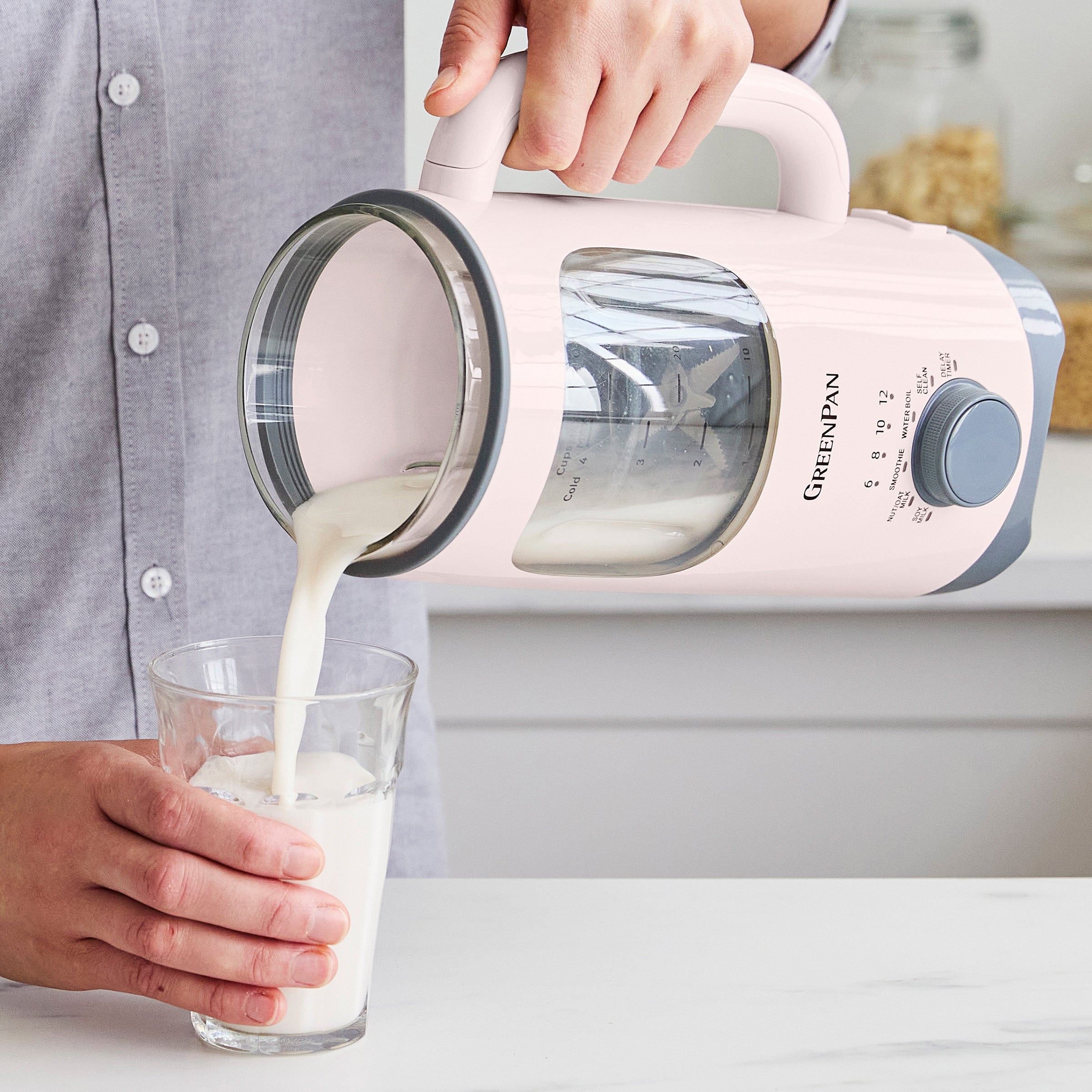 Person pouring milk from a pink GreenPan kitchen appliance into a glass.