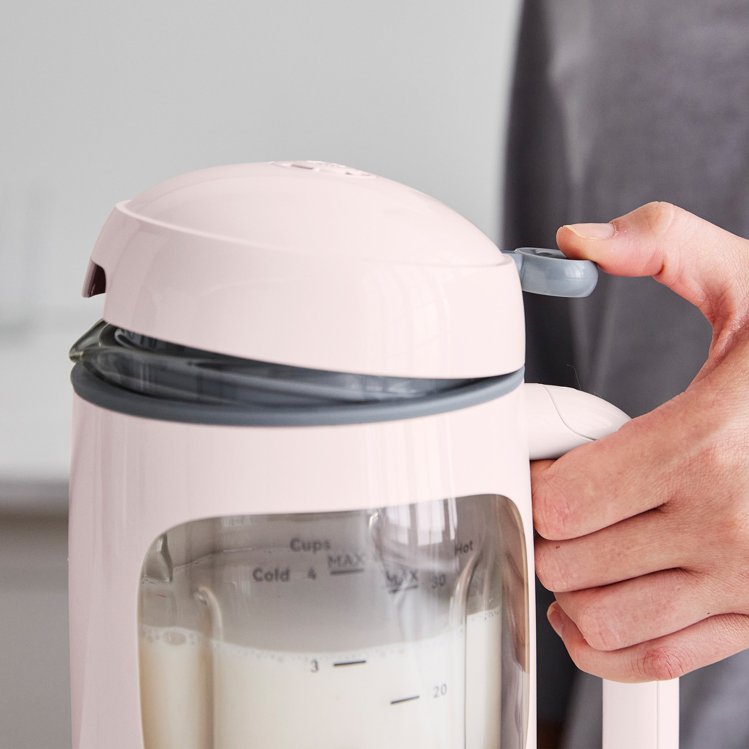 Person holding a pink kitchen appliance with milk inside, against a neutral background