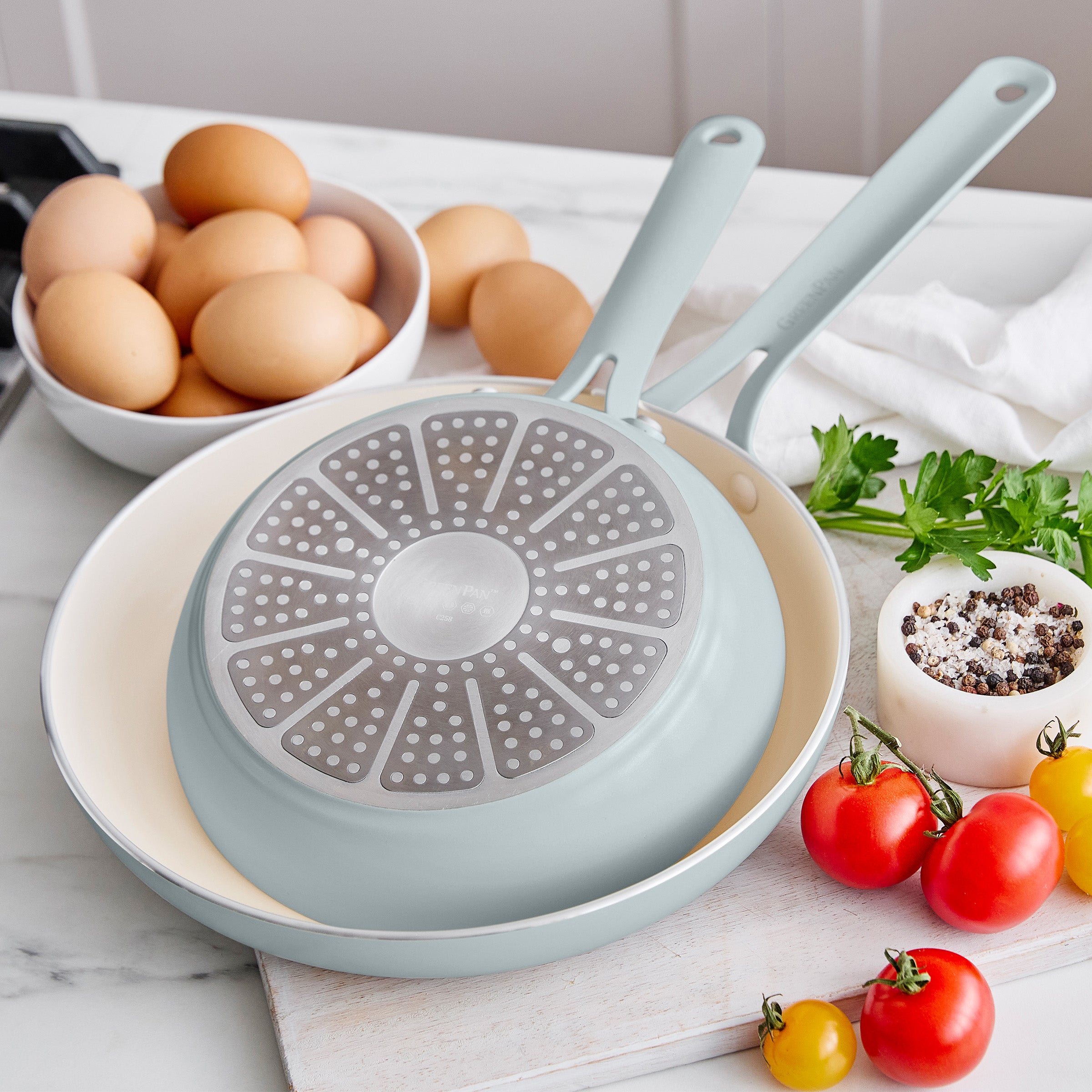 Light blue frying pan with a unique design on a kitchen counter with eggs and vegetables.