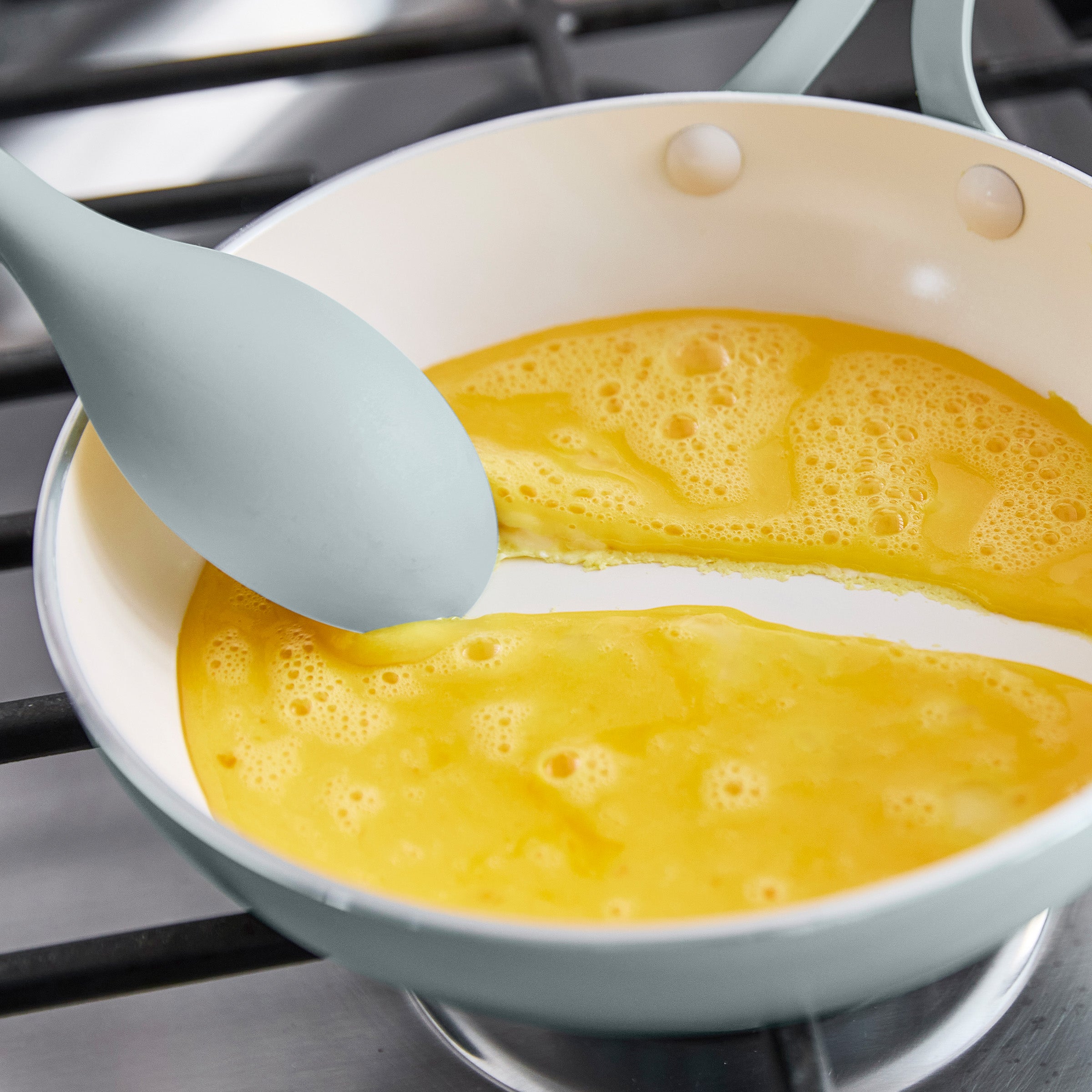 Spatula stirring eggs in a white pan on a stove