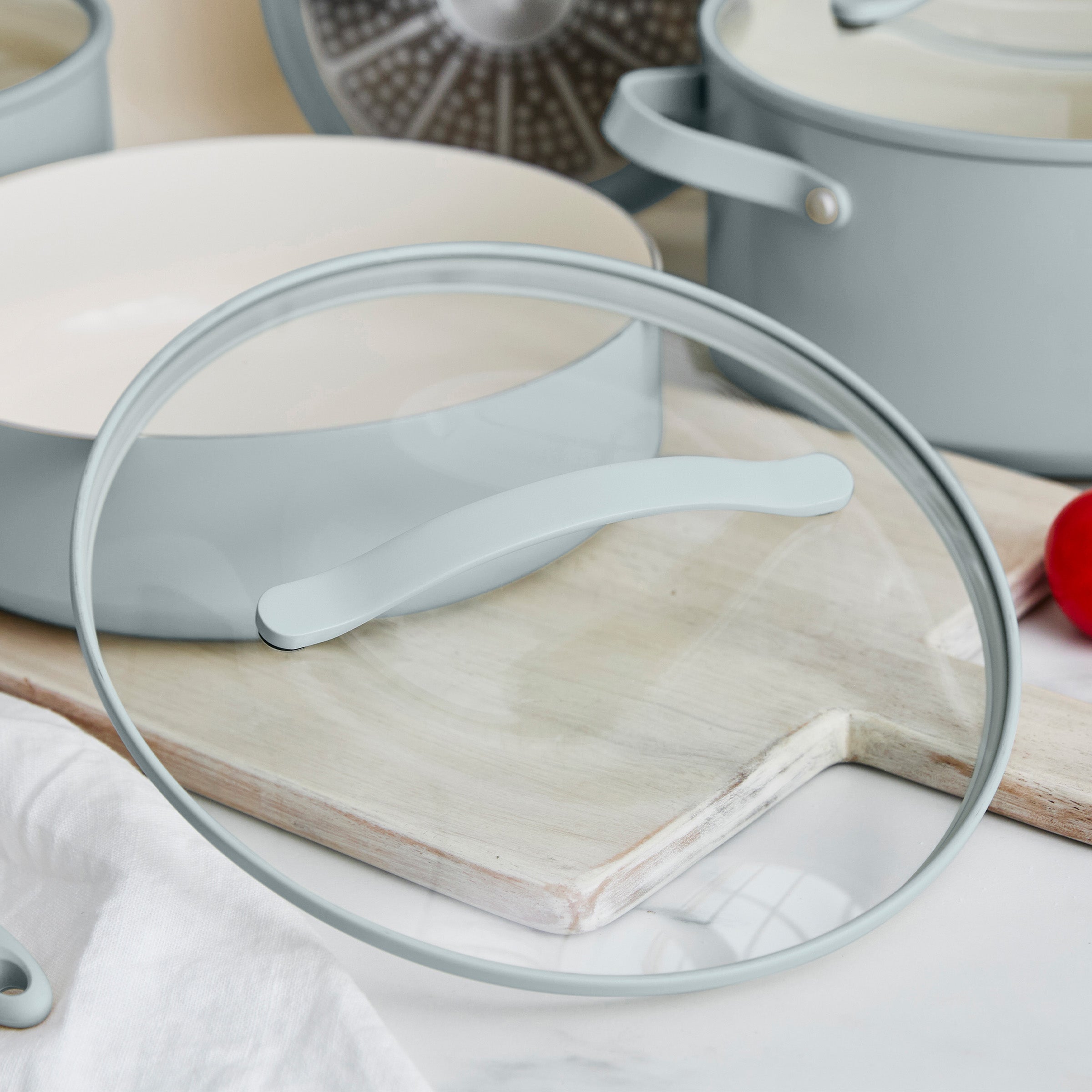 Blue cookware set with a glass lid on a wooden cutting board