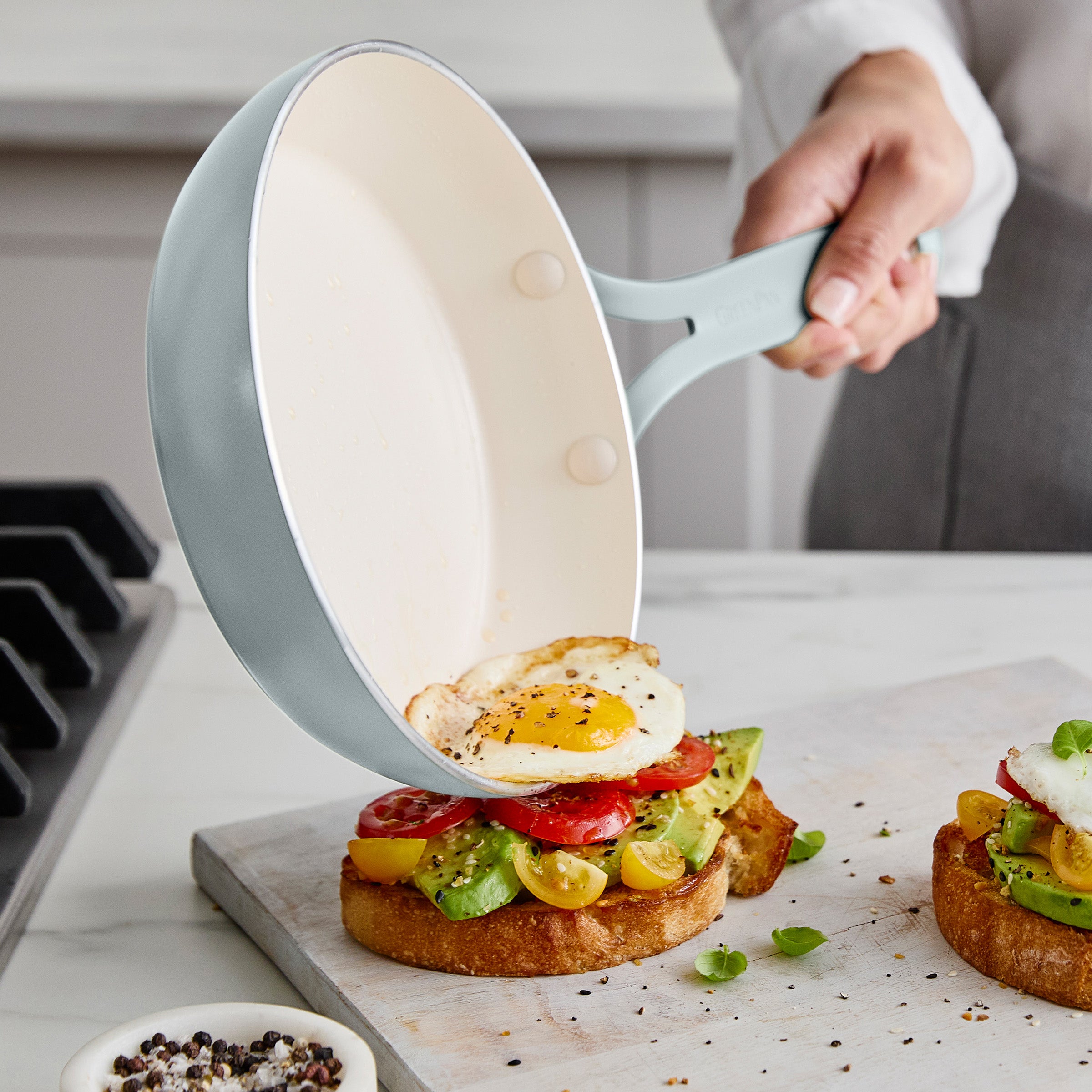 Person using a frying pan to place an egg on avocado toast