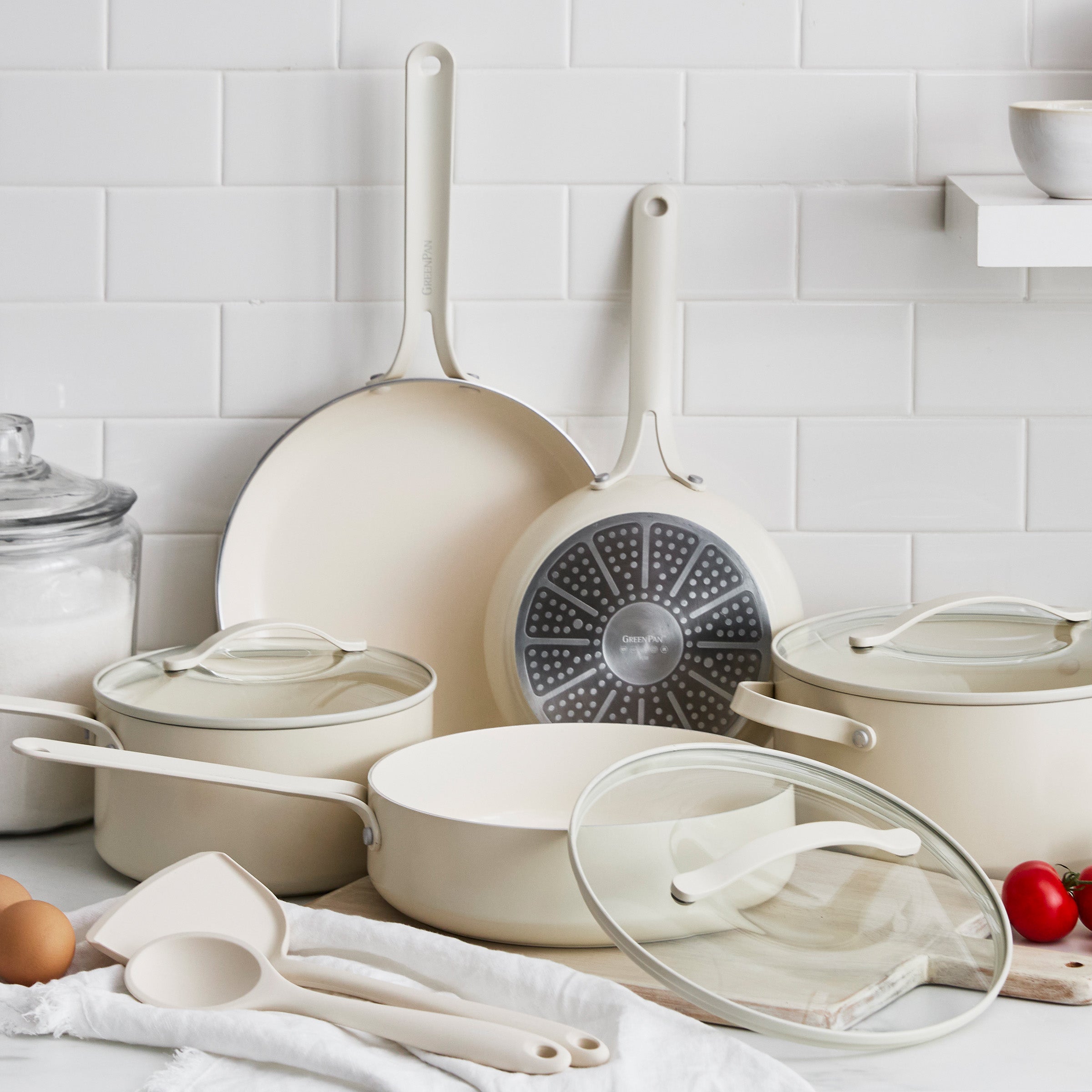 Set of cream-colored cookware including pots, pans, and lids on a kitchen counter.