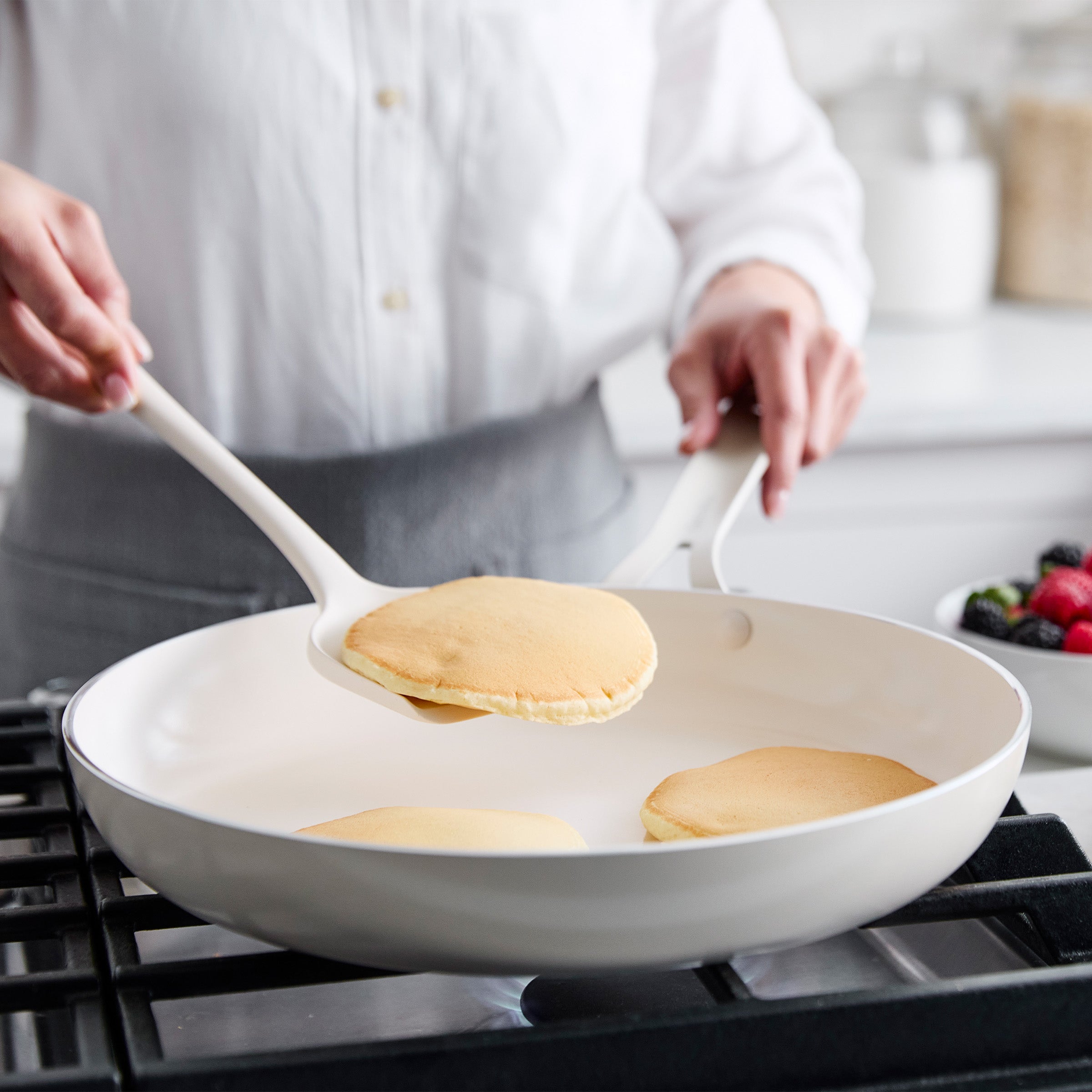 Person cooking pancakes in a cream pan on a stove