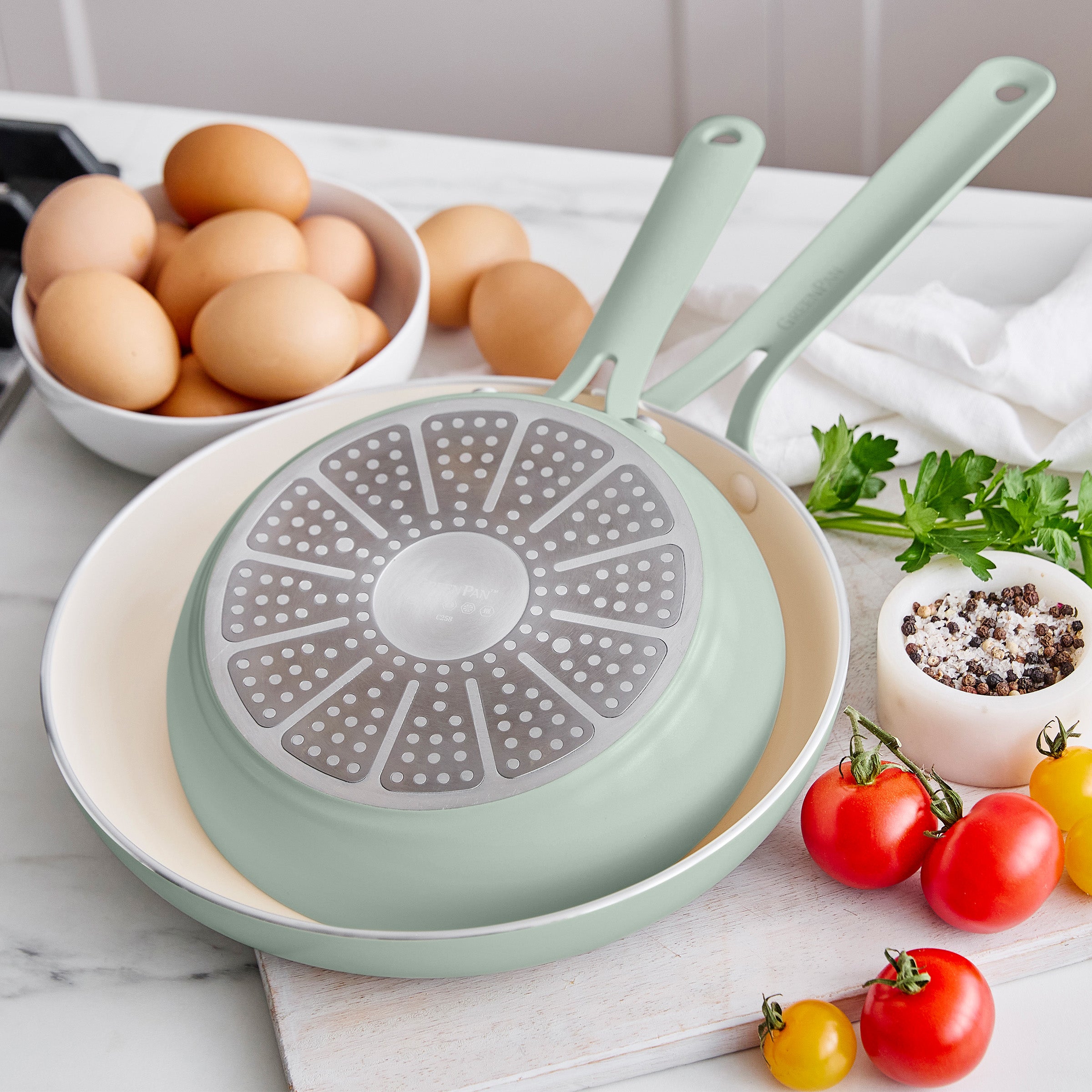 Green frying pan with a unique design on a kitchen counter with eggs and vegetables.