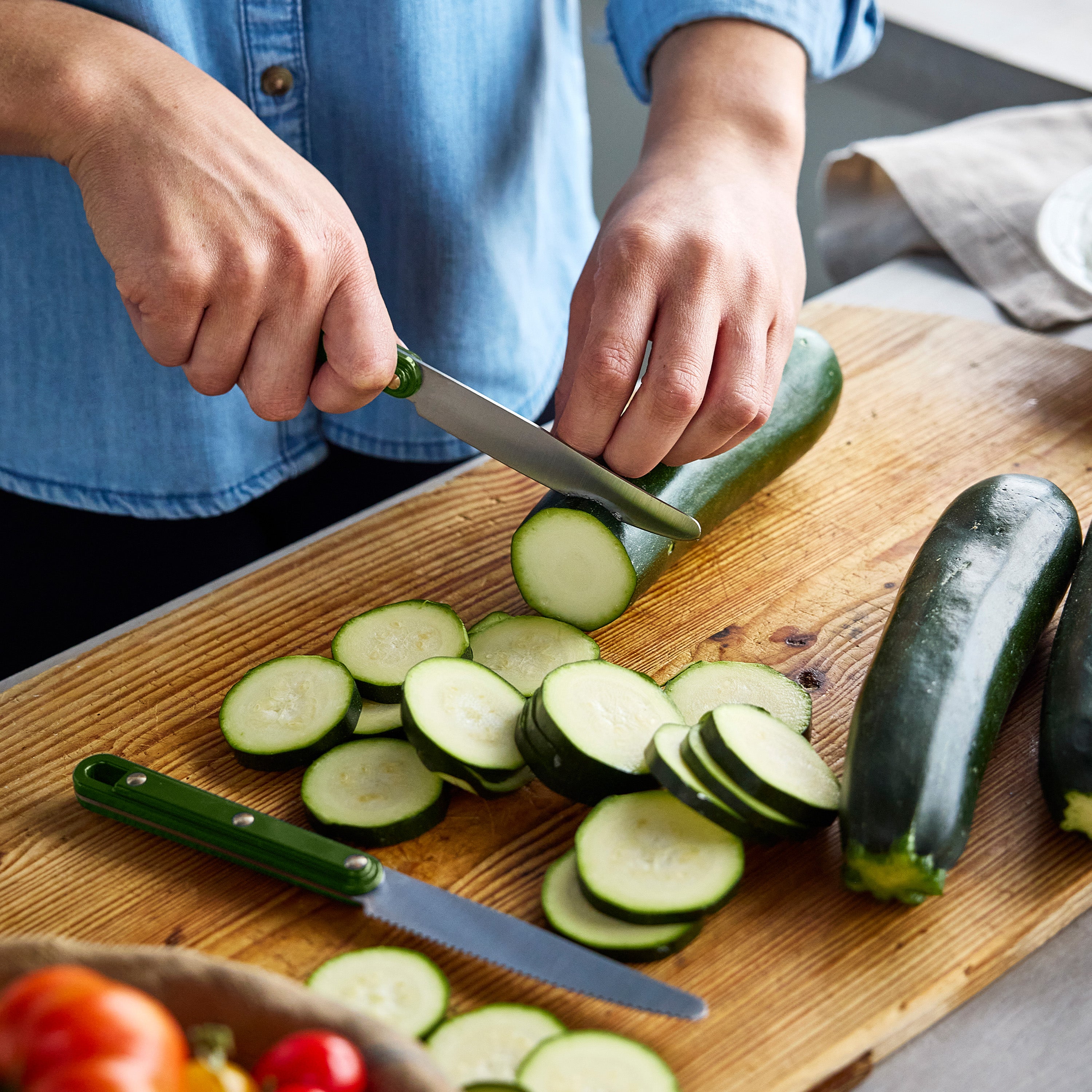 Person slicing zucchini on a wooden cutting board with a knife.