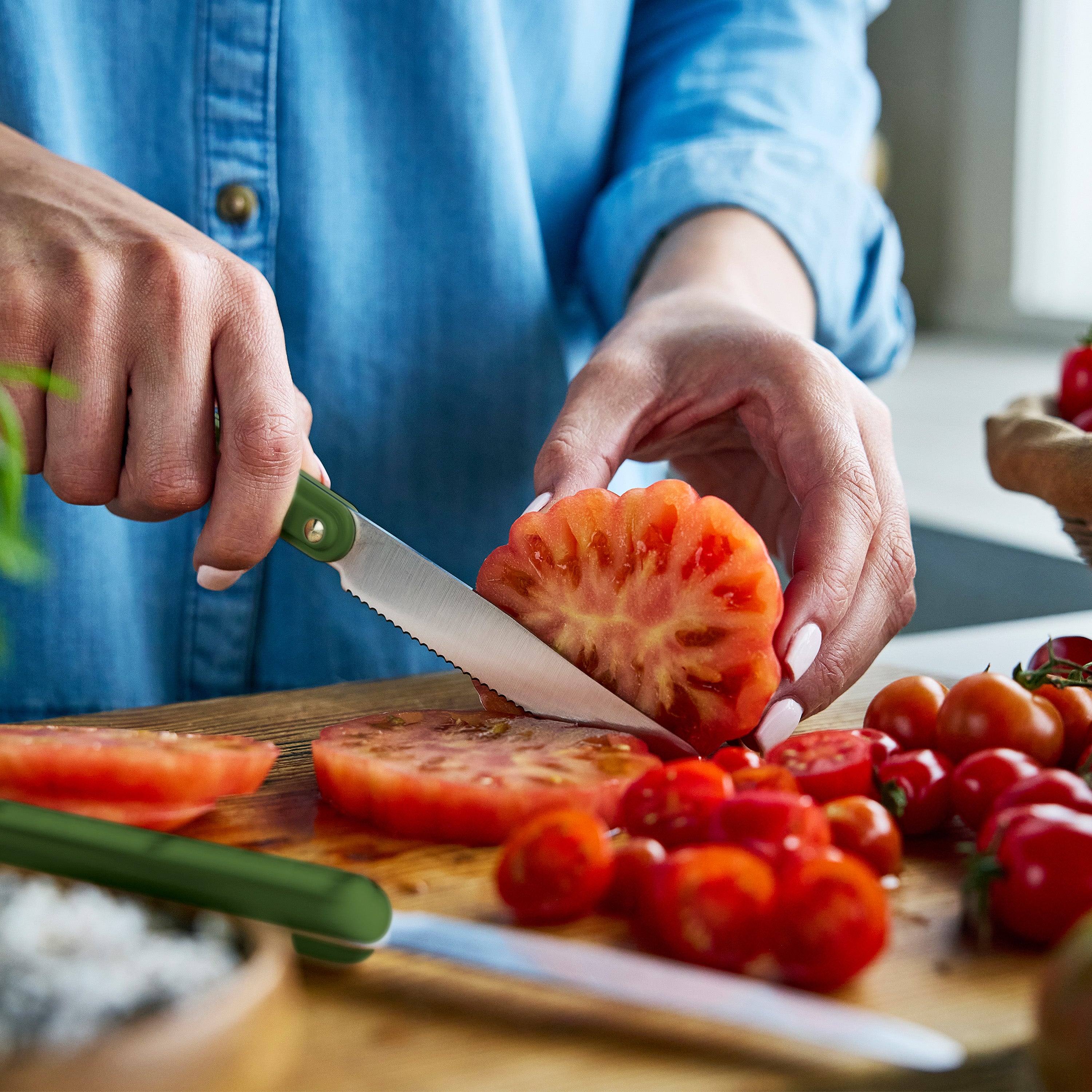 Person slicing tomato on a wooden cutting board with a knife.