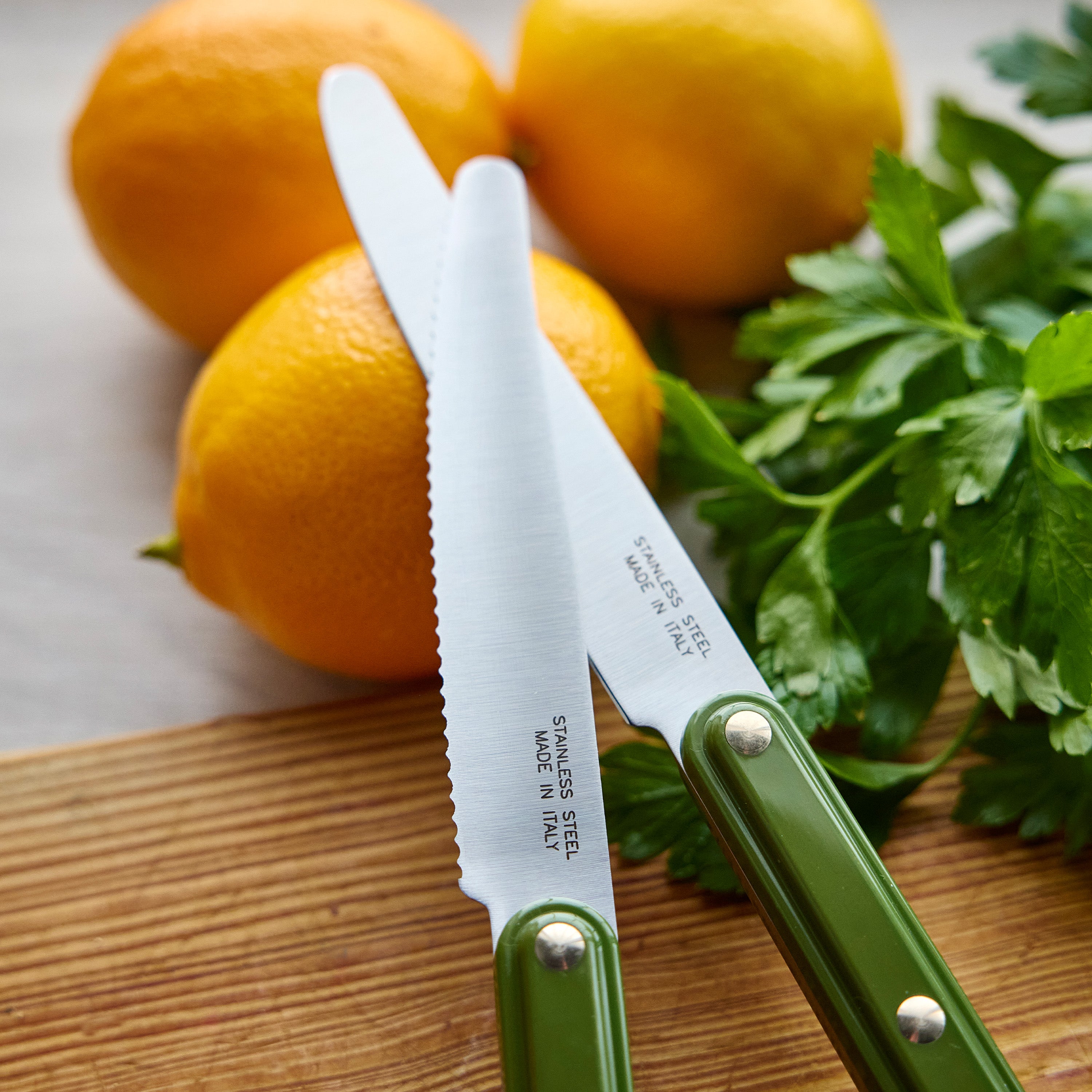 Two knives with green handles on a wooden cutting board with citrus and herbs