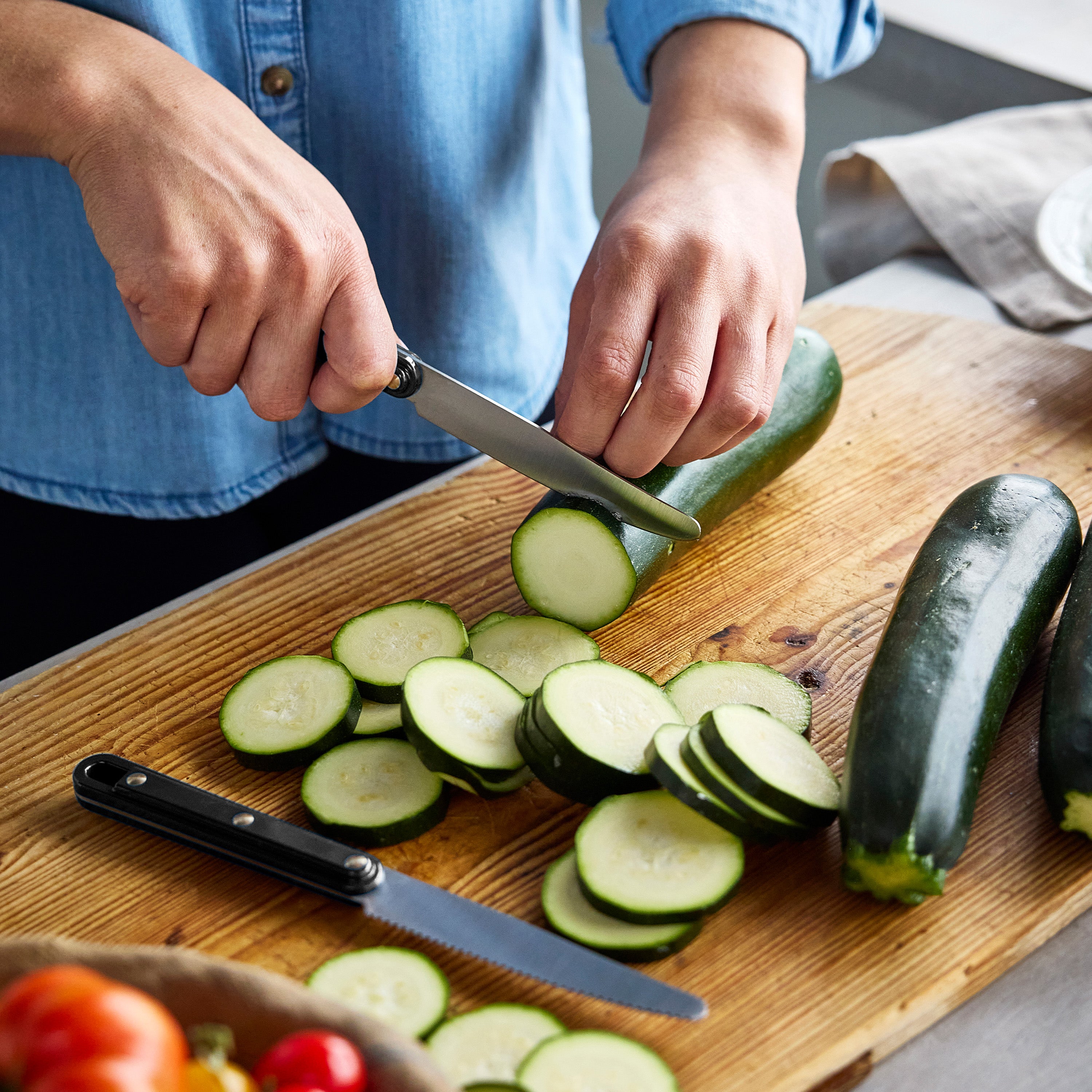 Person slicing zucchini on a wooden cutting board with a knife.