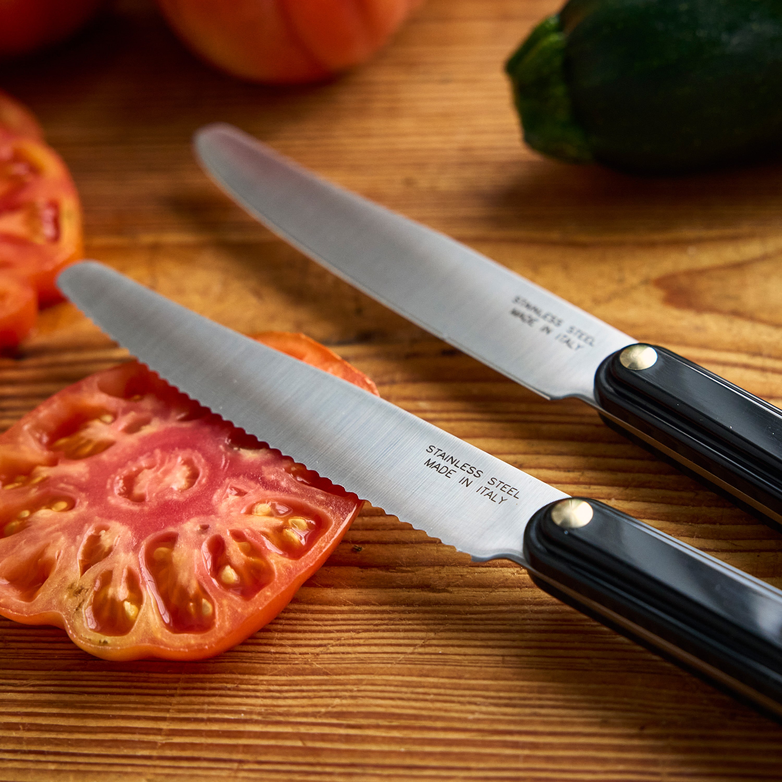 Two knives on a wooden cutting board with zucchini and tomatoes, featuring the brand 'Tucci'