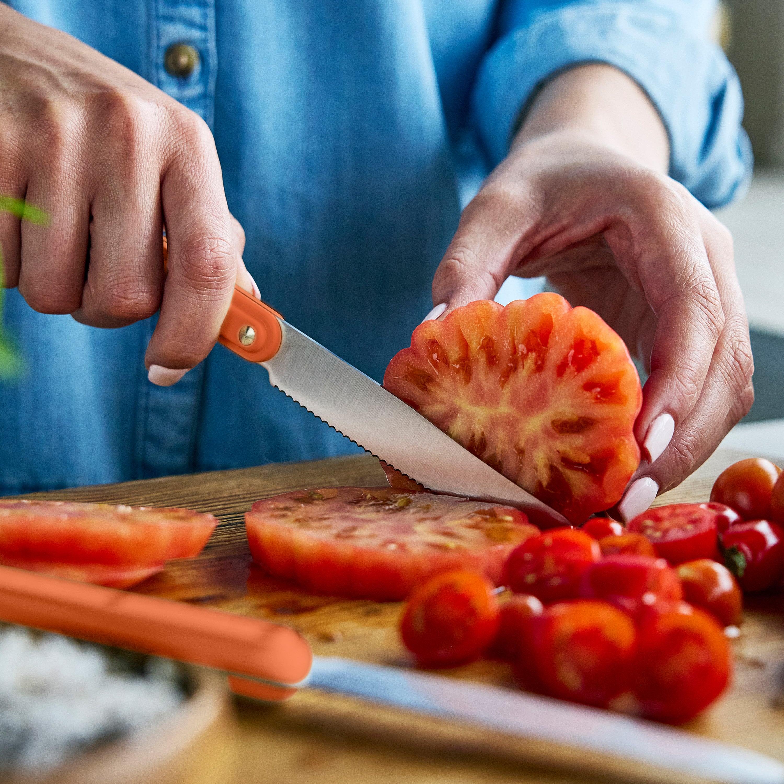 Person slicing tomato on a wooden cutting board with a knife.