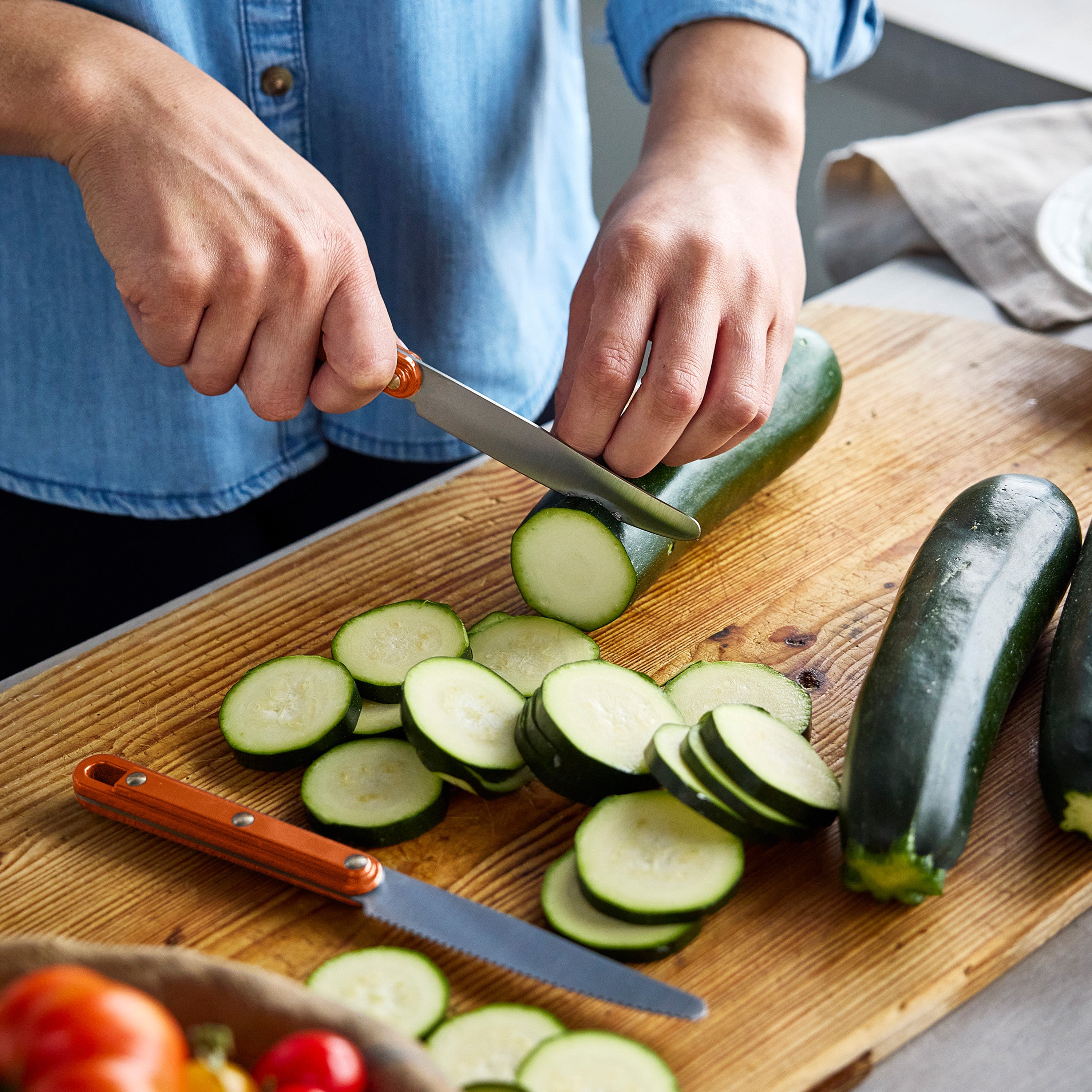 Person slicing zucchini on a wooden cutting board with a knife.