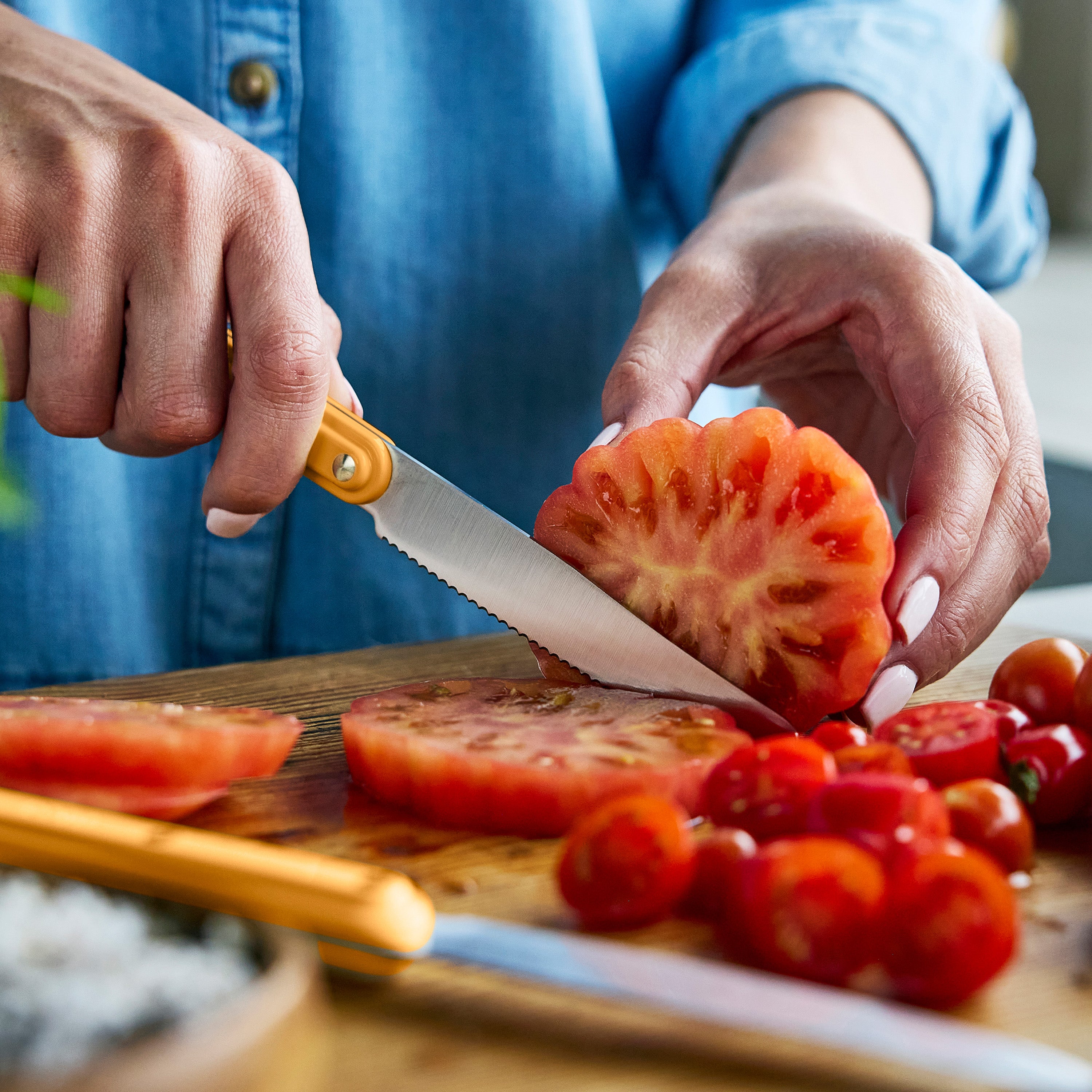 Person slicing tomato on a wooden cutting board with a knife.