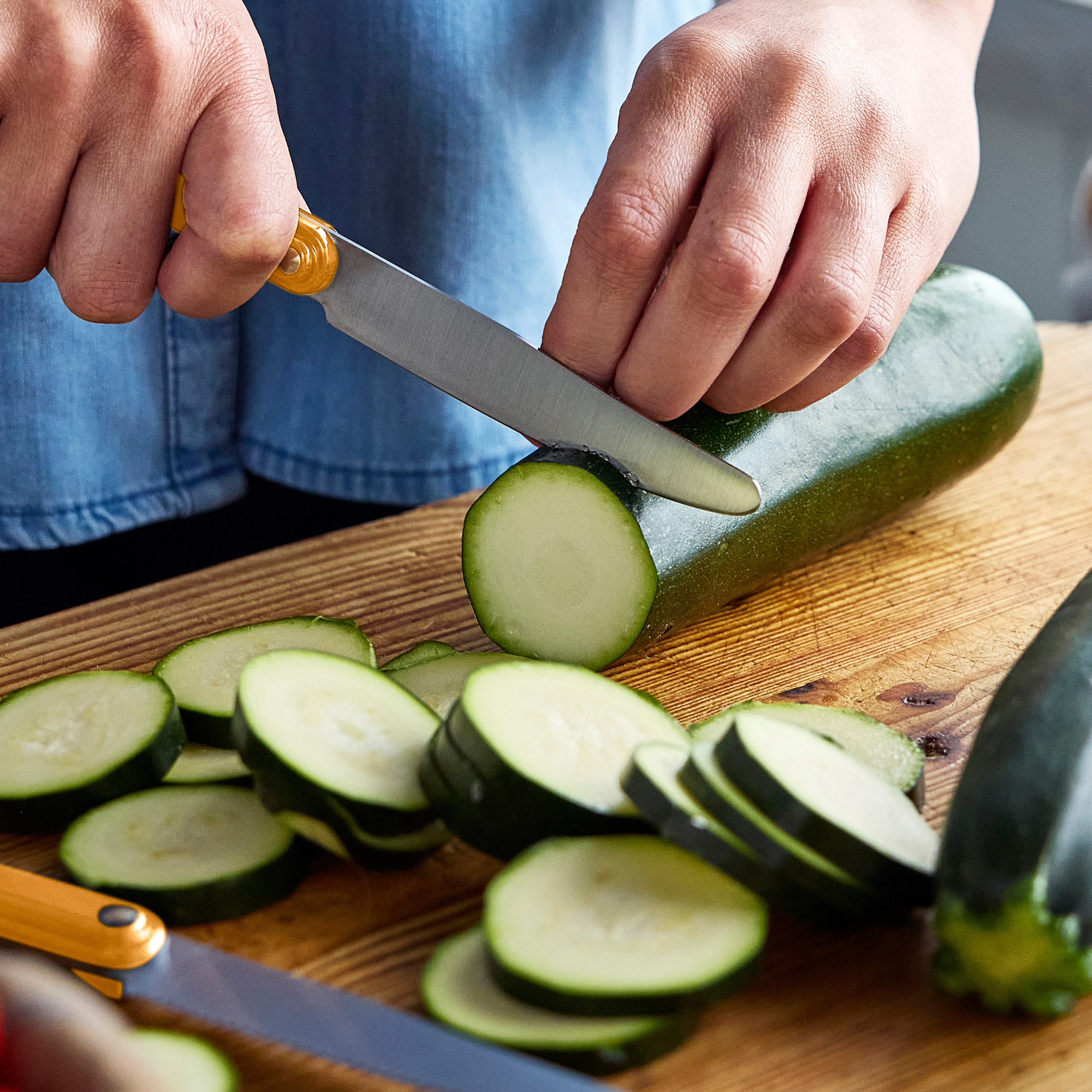 Person slicing zucchini on a wooden cutting board with a knife.