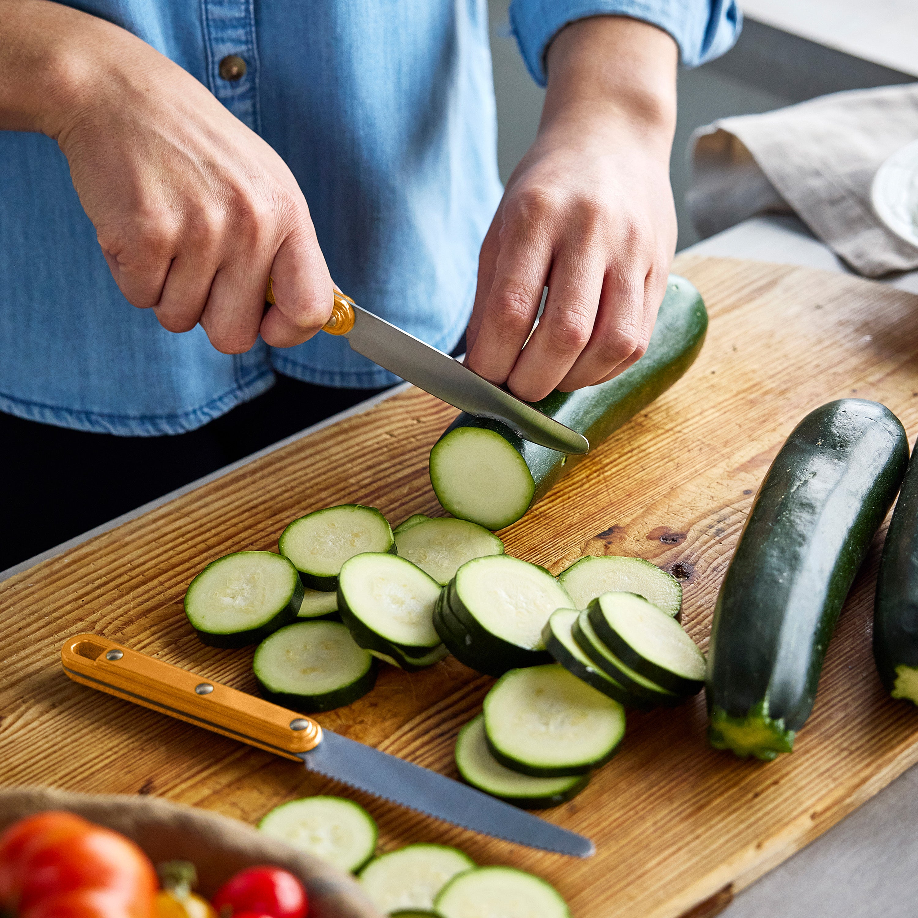 Person slicing zucchini on a wooden cutting board with a knife.