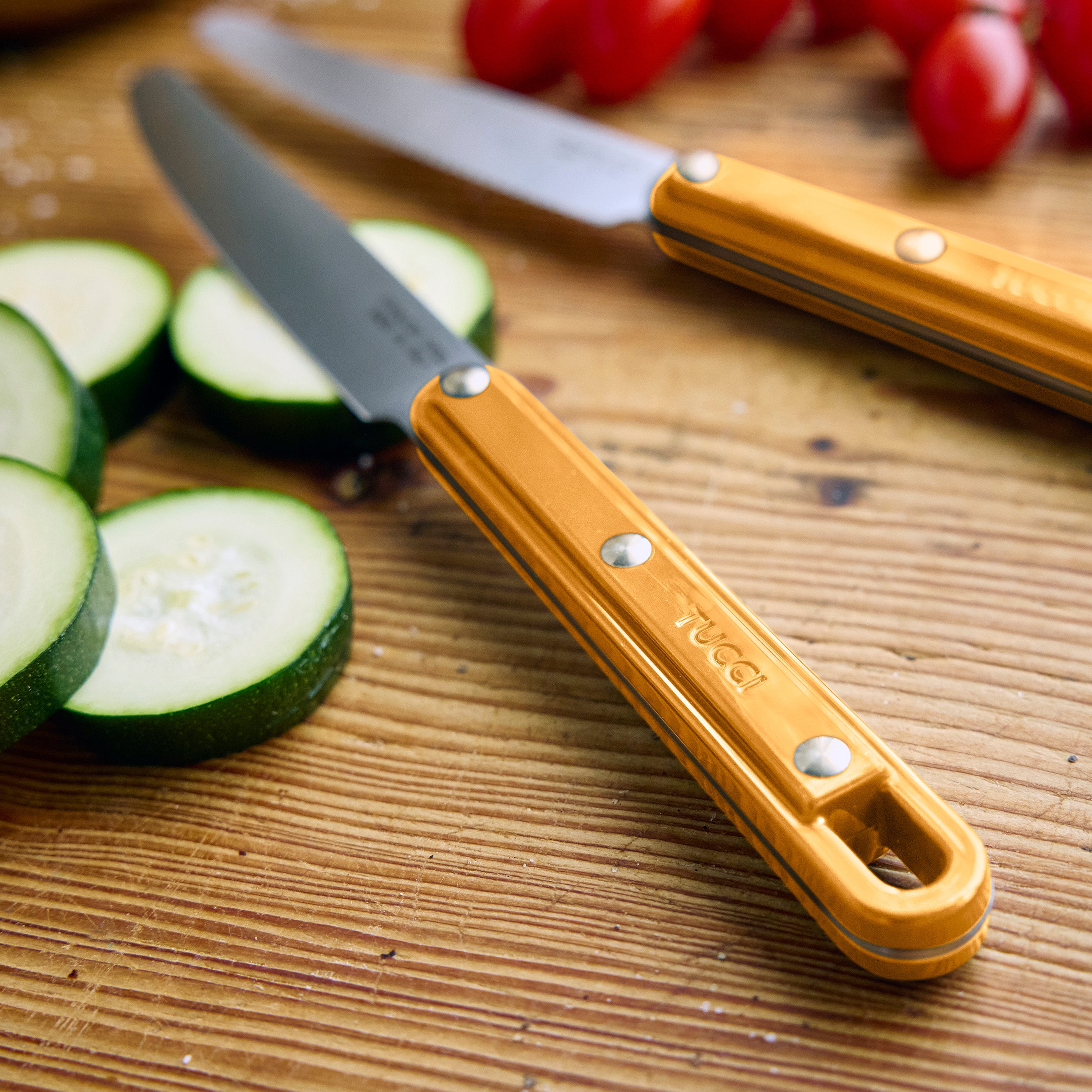 Two knives with yellow handles on a wooden cutting board with zucchini and tomatoes