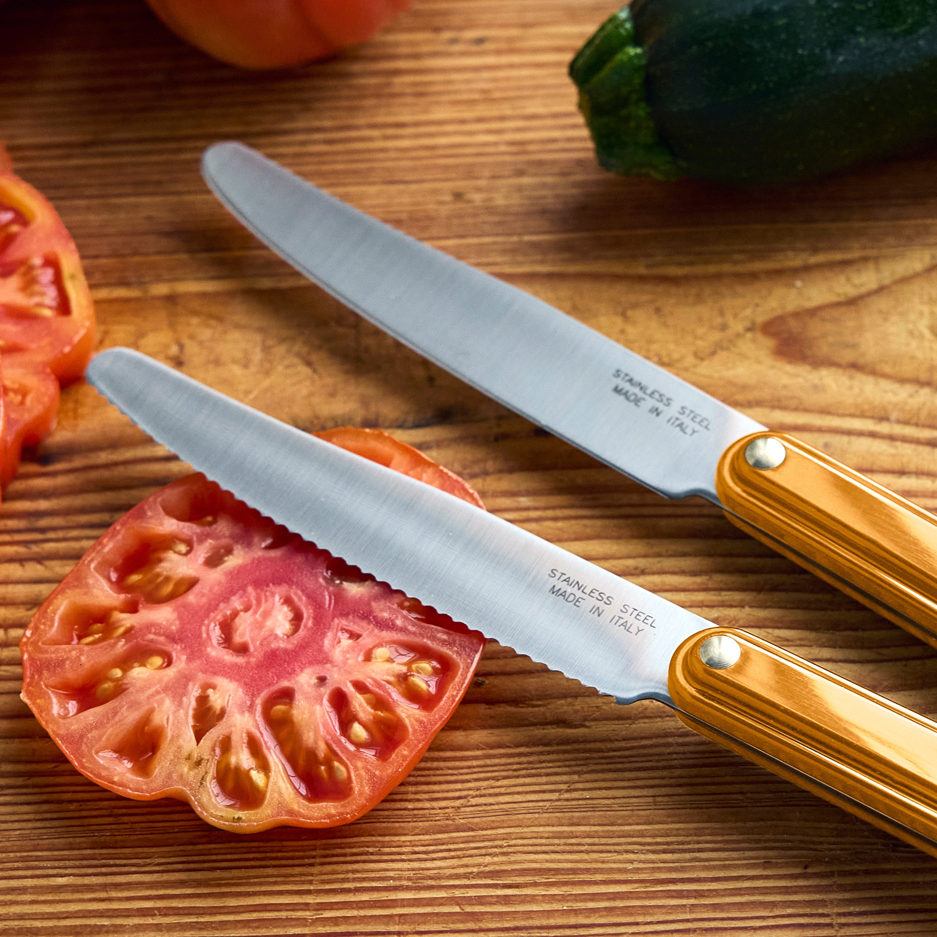 Two knives on a wooden cutting board with sliced zucchini and tomatoes, featuring the brand 'Tucci'