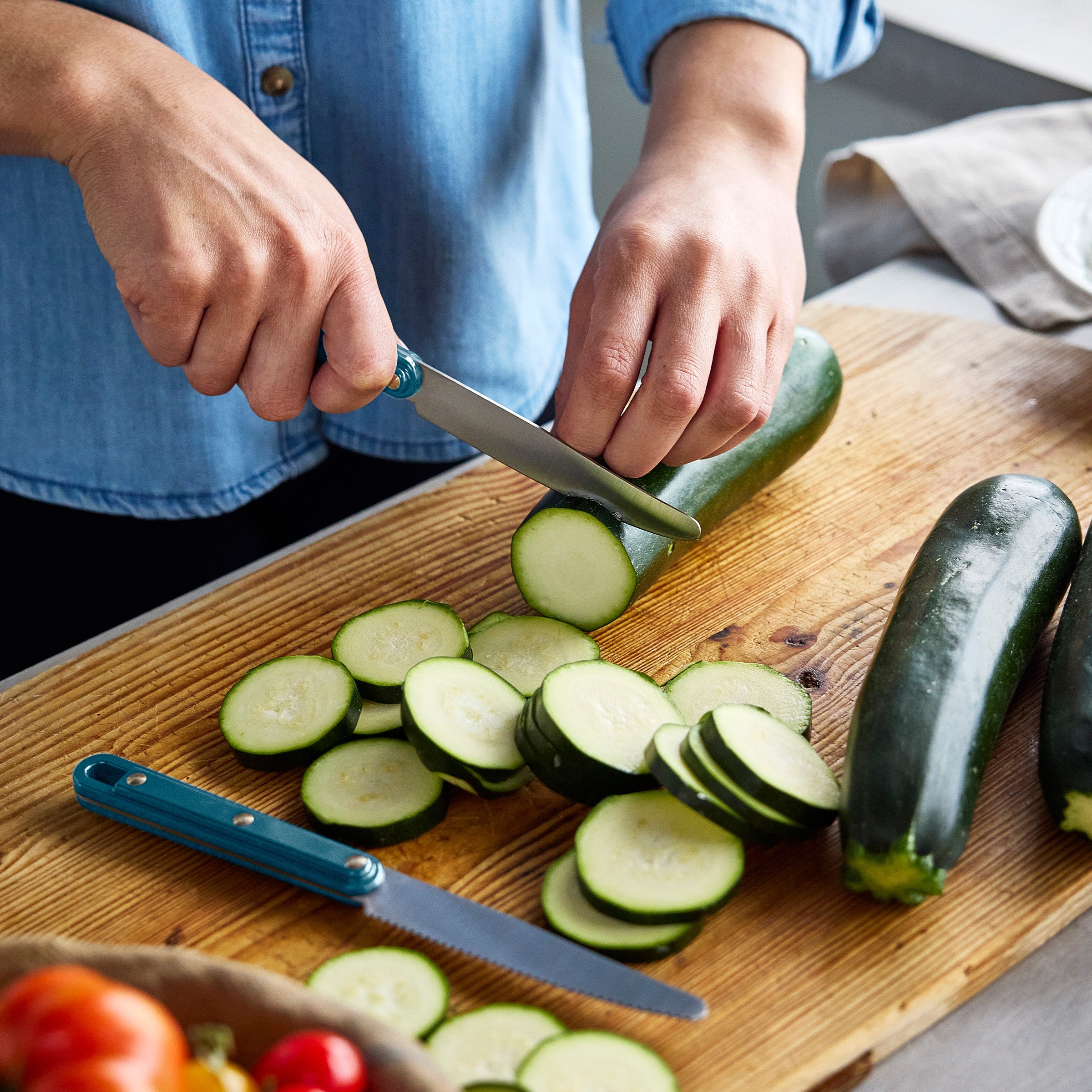 Person slicing zucchini on a wooden cutting board with a knife.