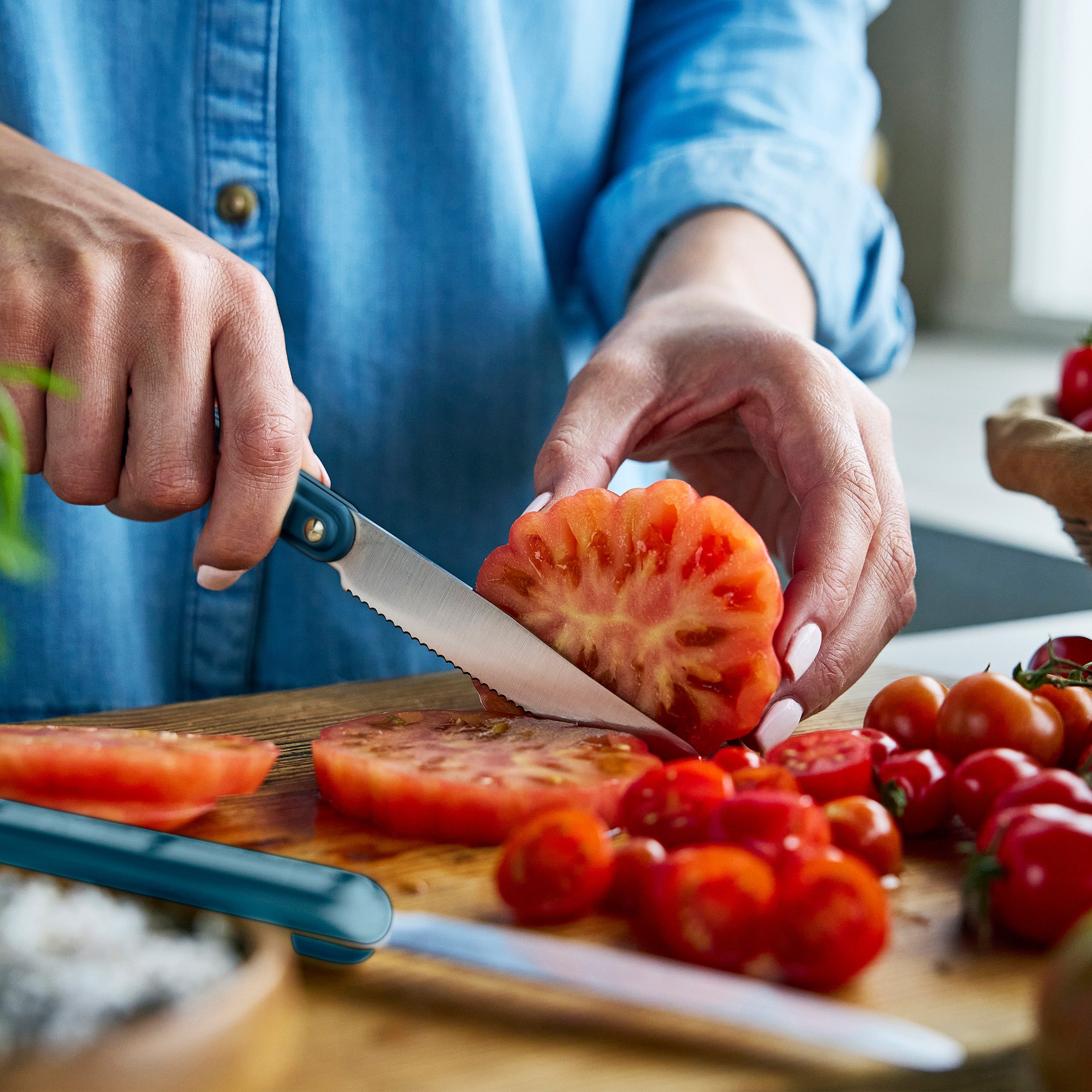 Person slicing tomato on a wooden cutting board with a knife.