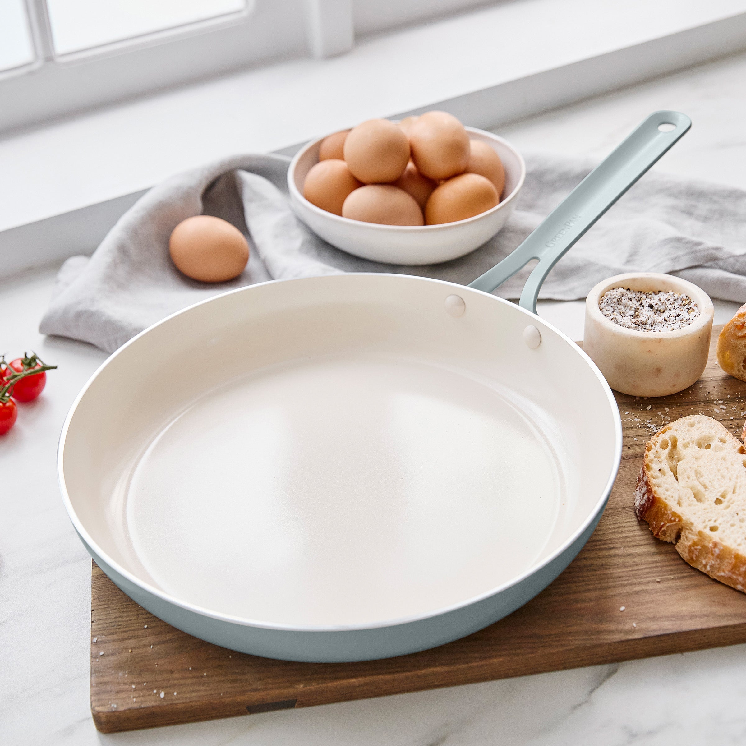 Blue frying pan on a marble countertop with eggs and bread in the background