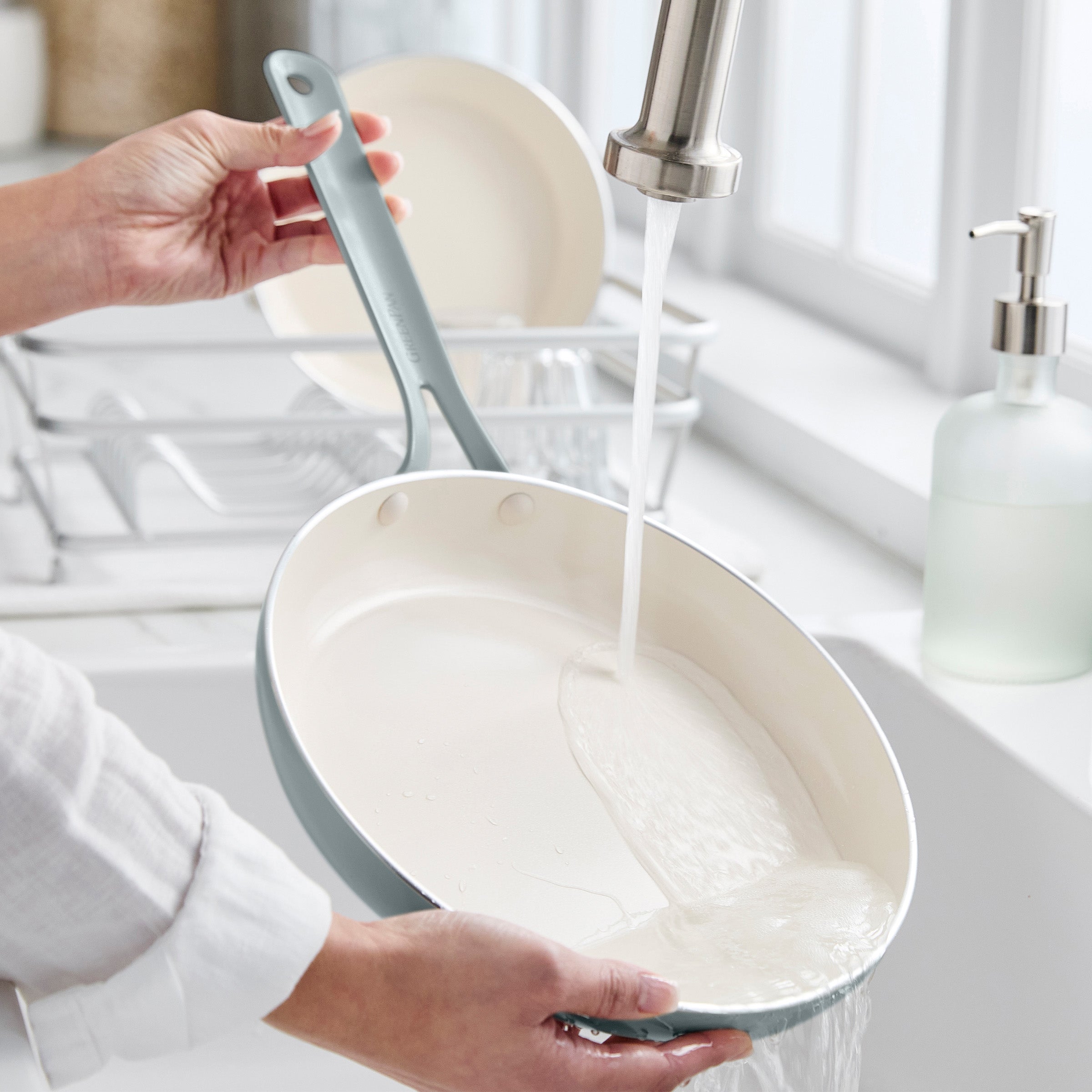 Person washing a frying pan under running water in a kitchen sink