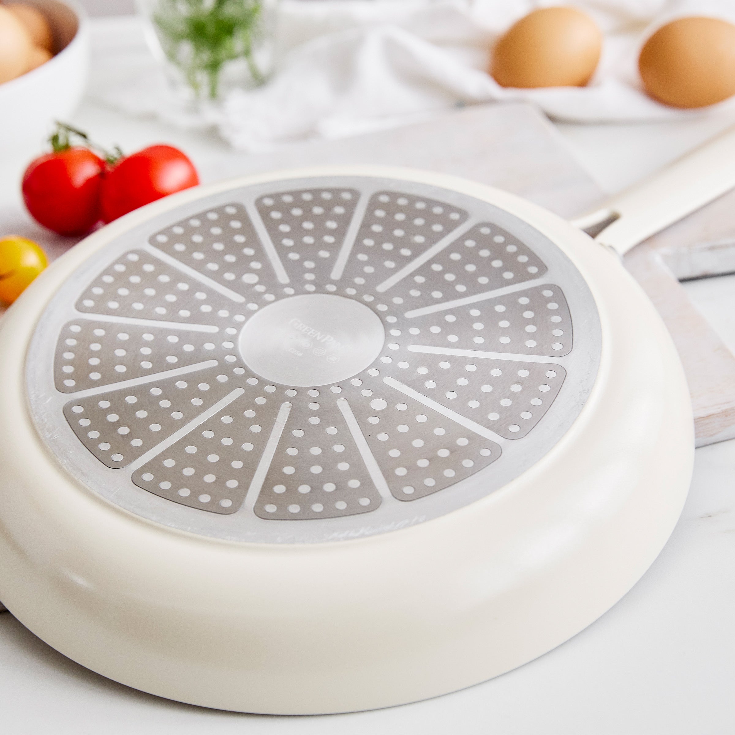 Frypan with perforated design on a white surface with eggs and tomatoes.