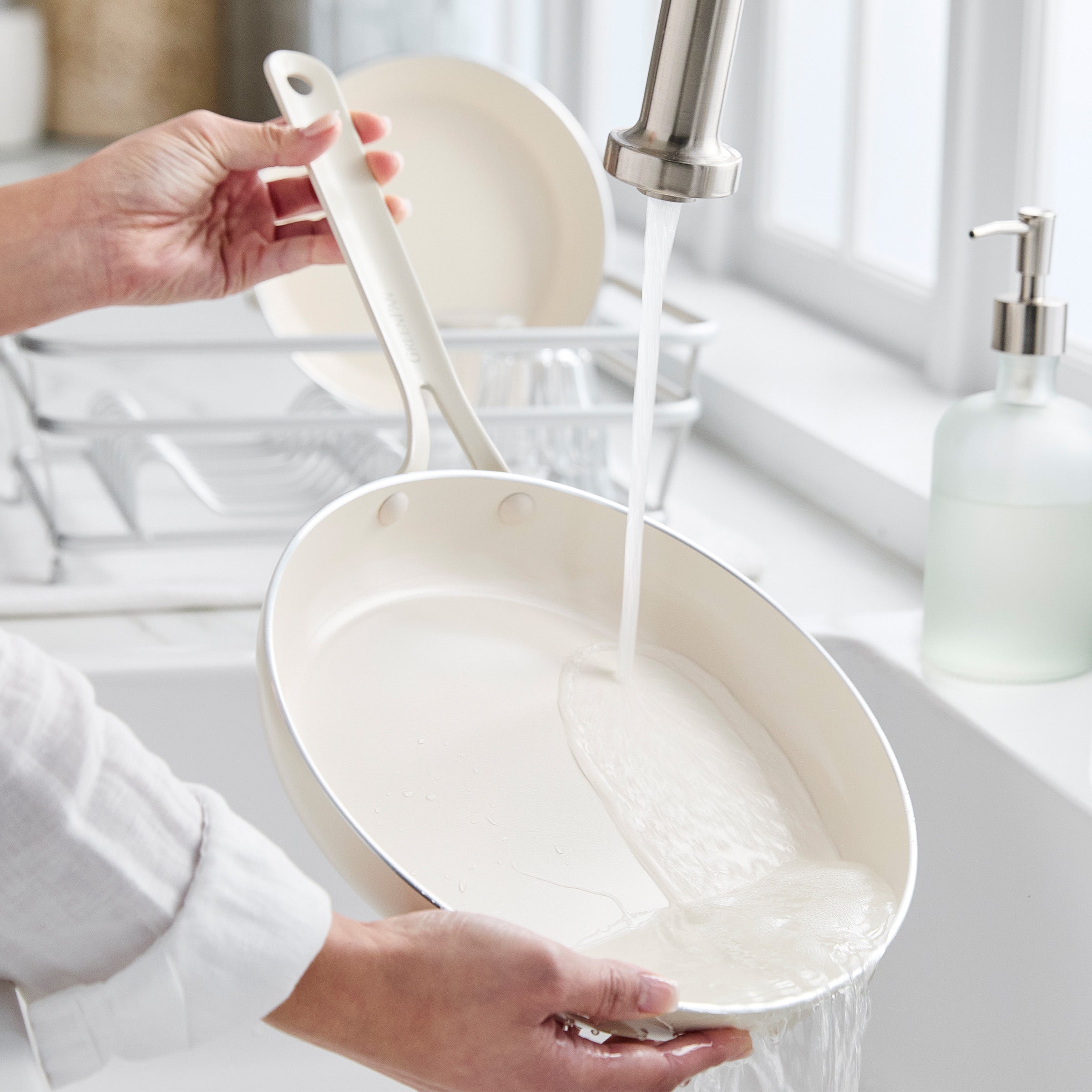 Person washing a white frying pan under running water in a kitchen sink