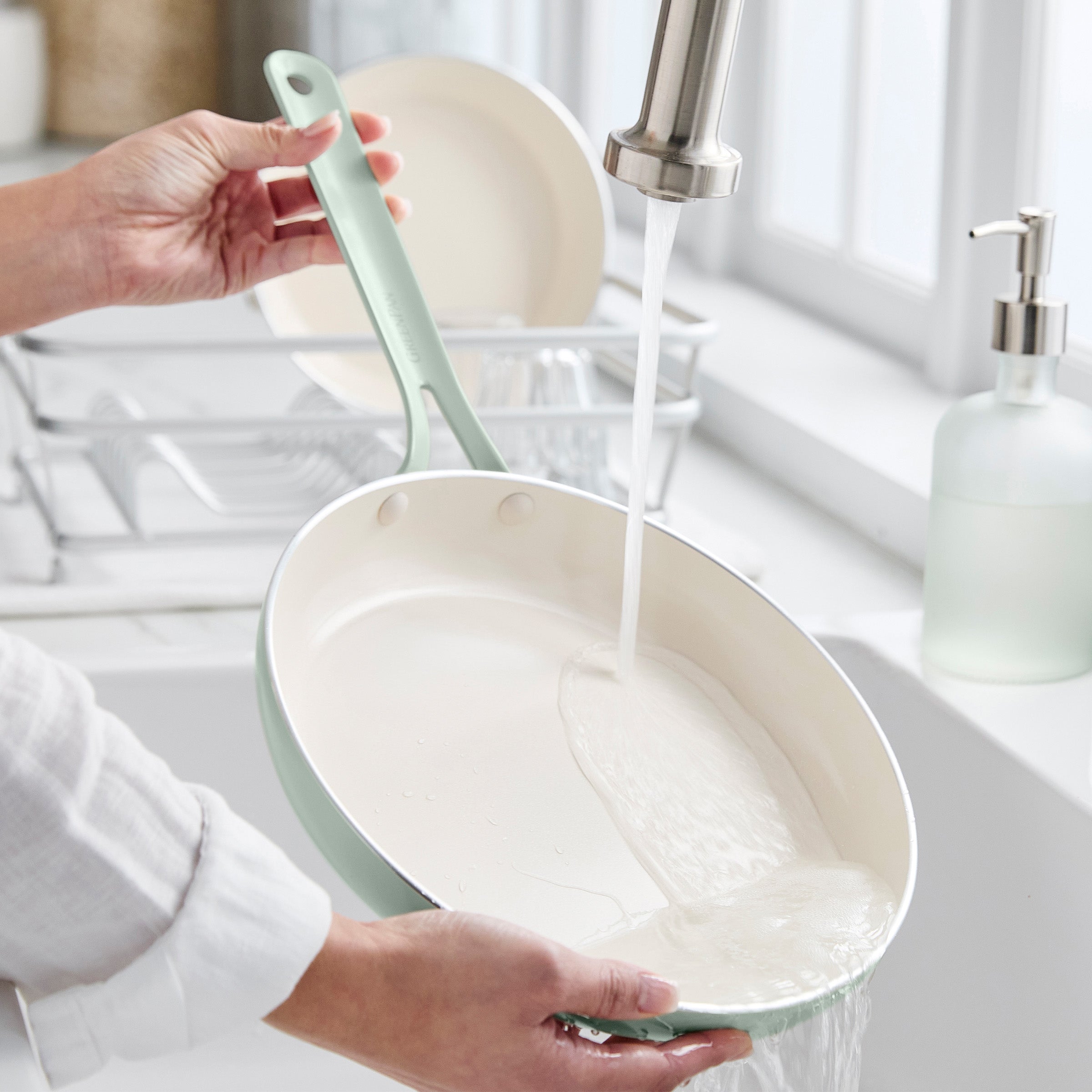 Person washing a green frying pan under running water in a kitchen sink