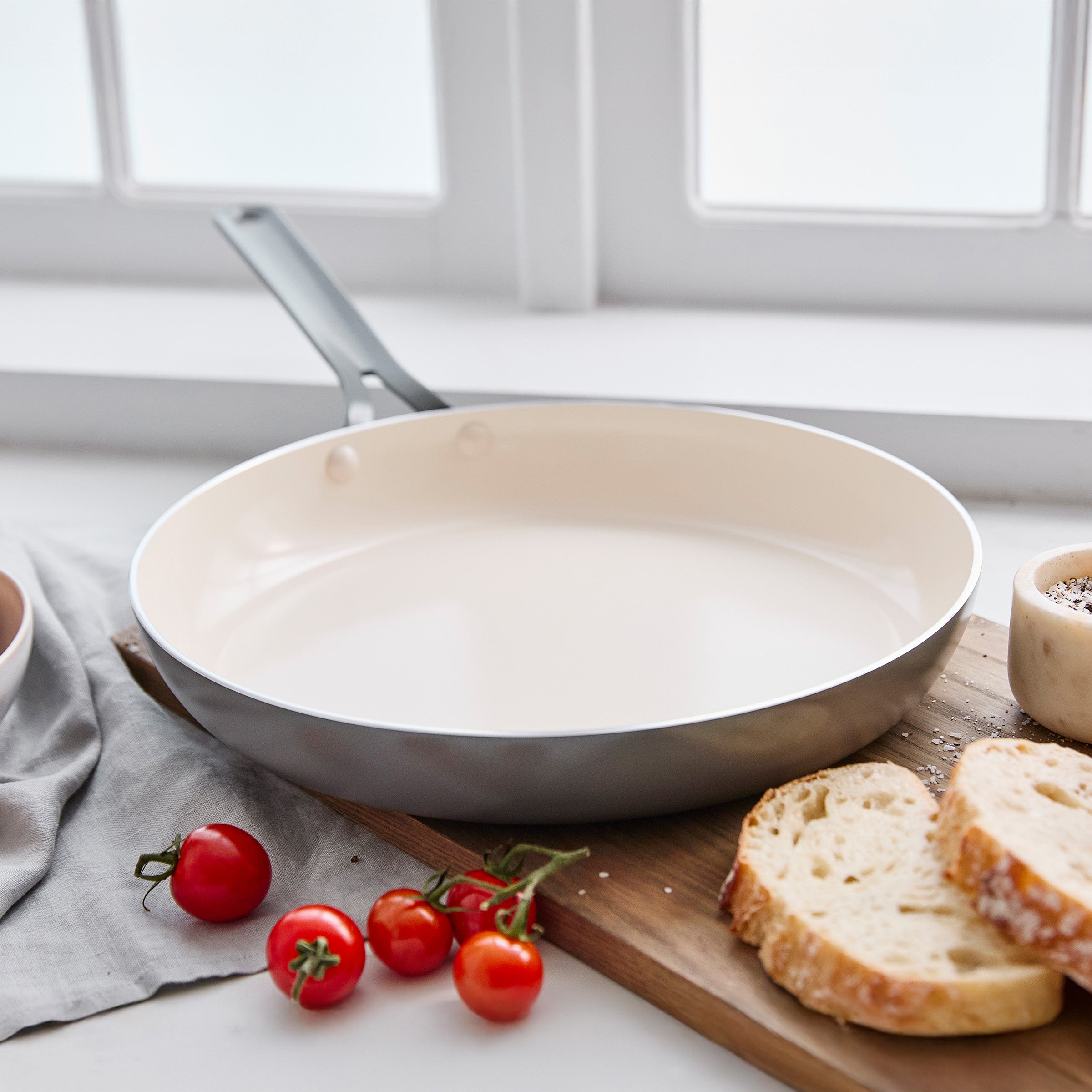 Gray frying pan on a kitchen counter with bread and tomatoes