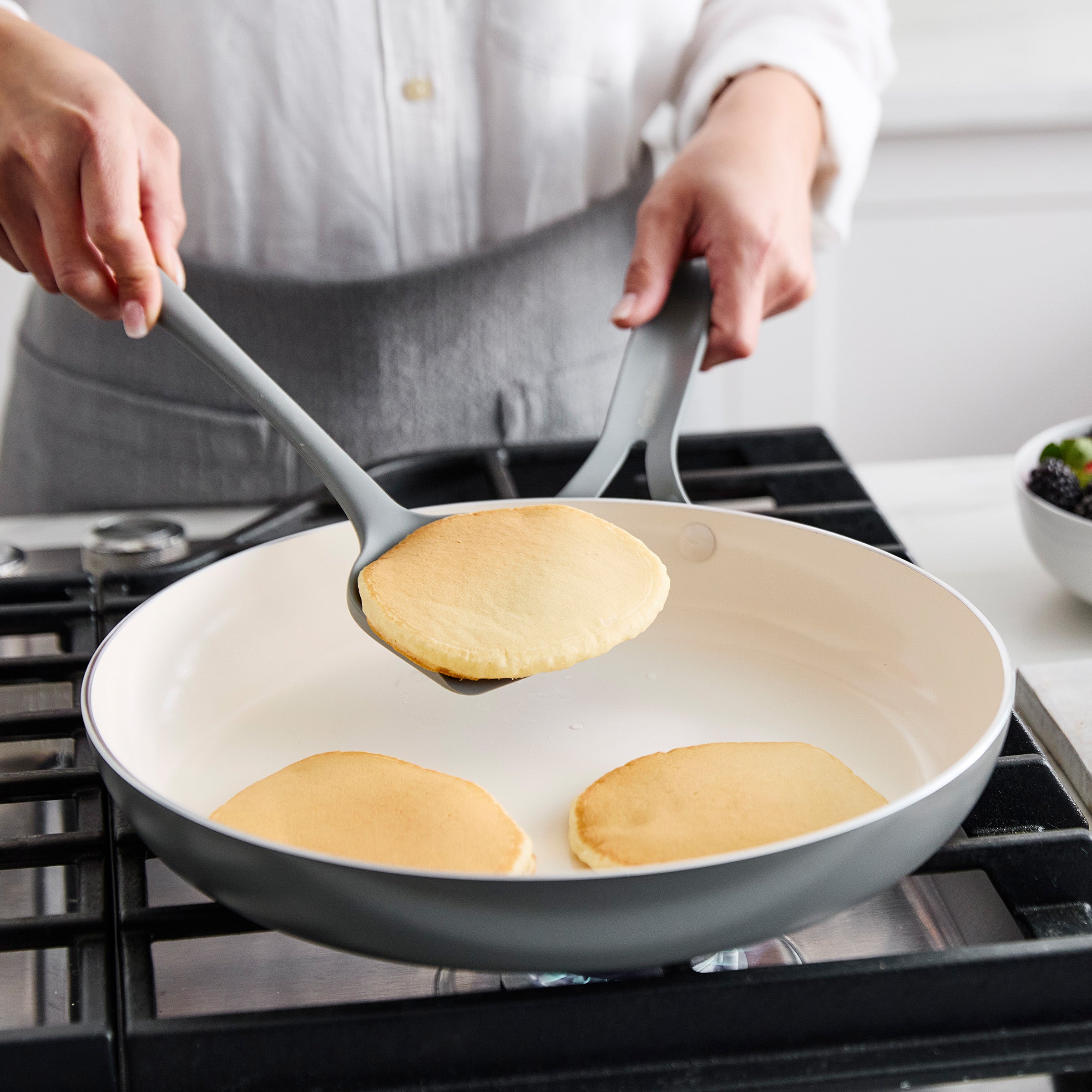 Person flipping pancakes in a pan on a stove