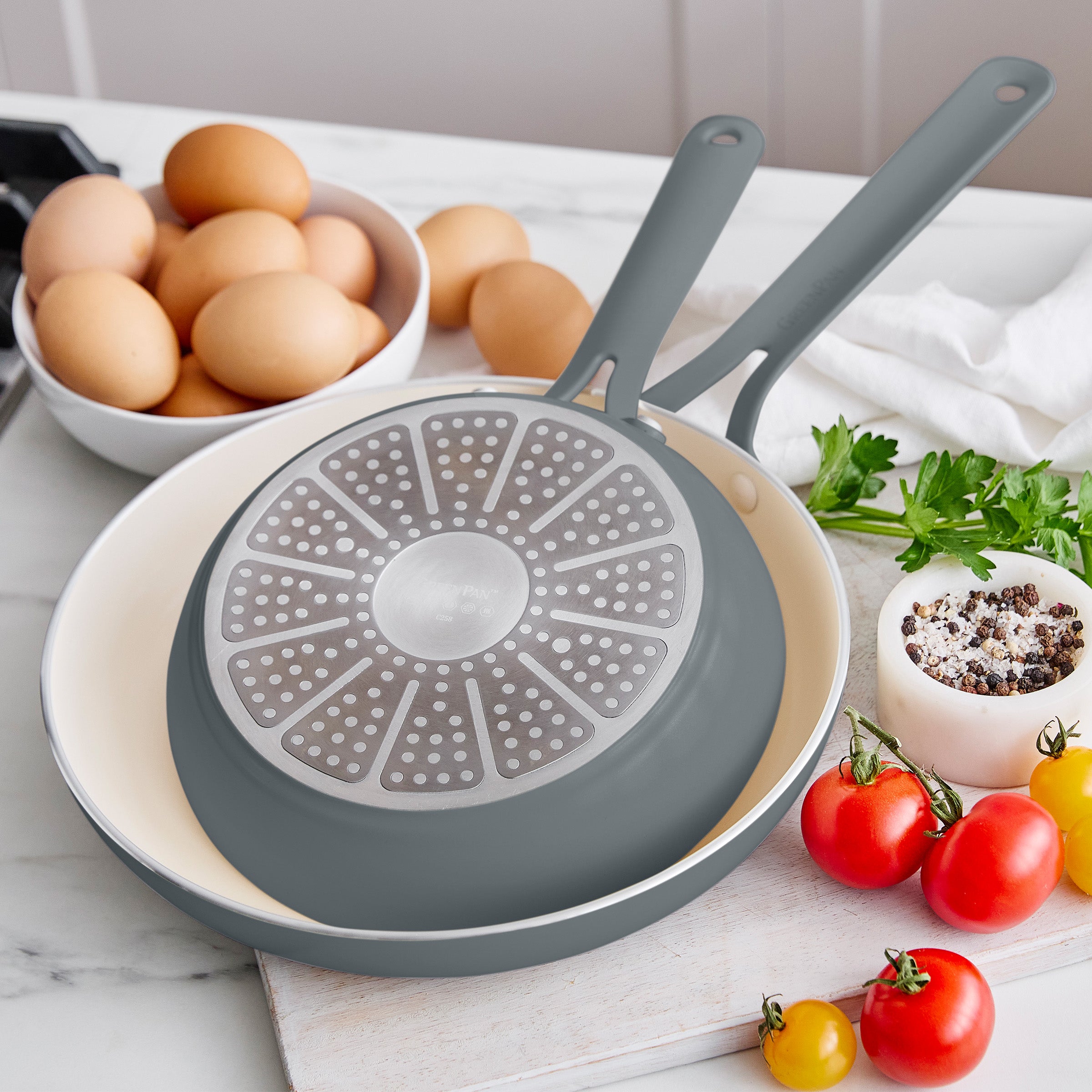 Gray frying pan with a unique design on a kitchen counter with eggs and vegetables.