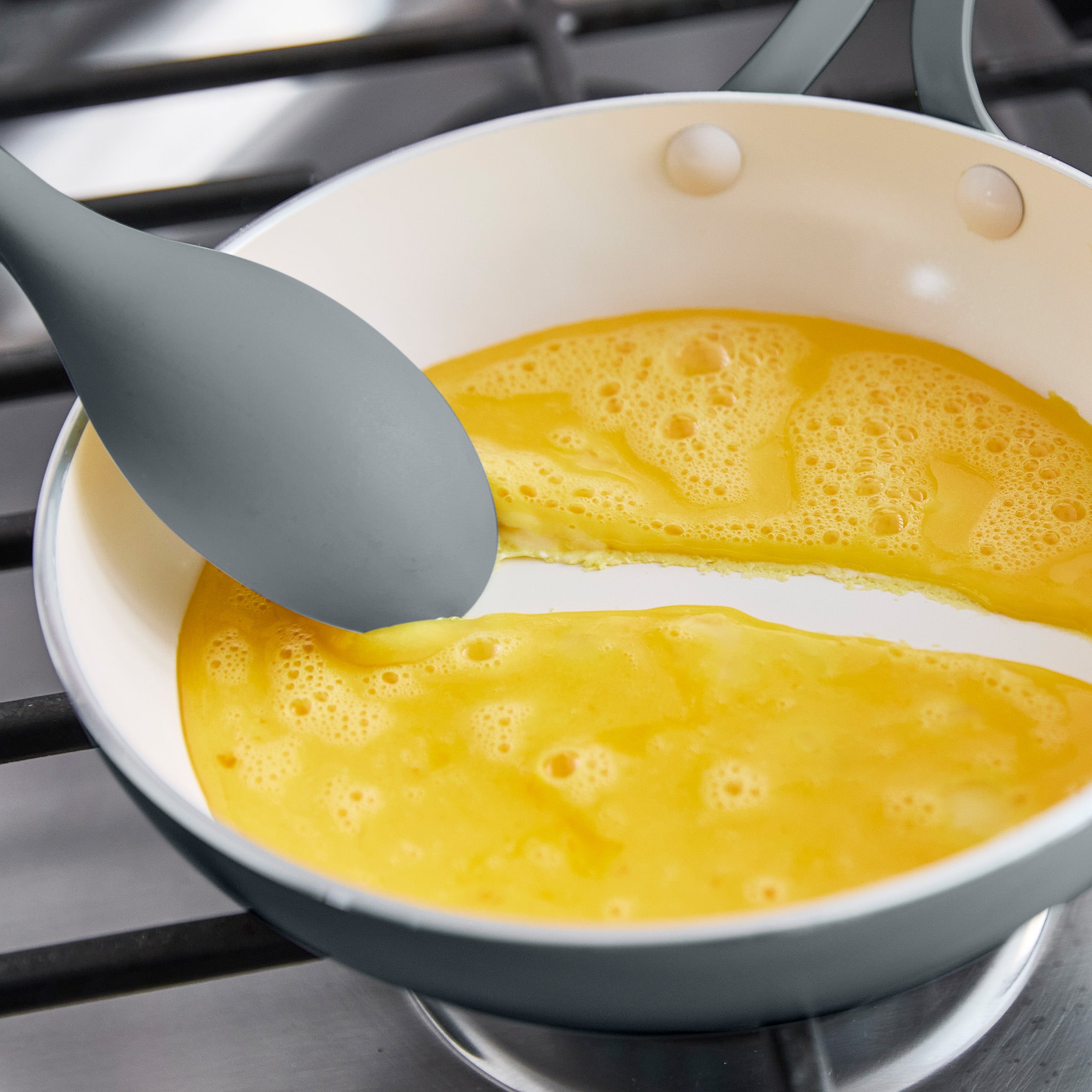 Frying pan with scrambled eggs and a gray spoon on a stove.