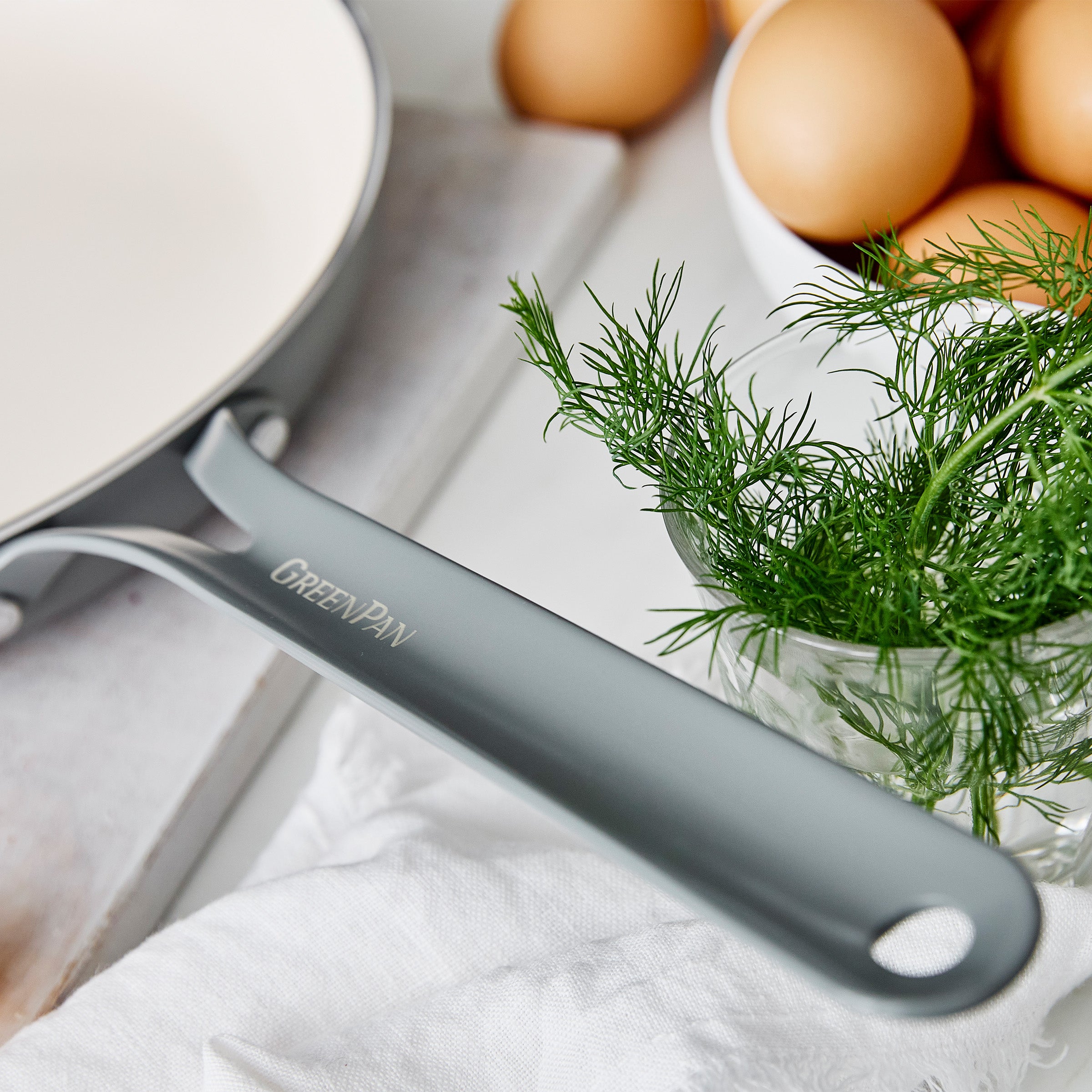 Gray frying pan with 'GreenPan' branding on a kitchen counter with eggs and dill.